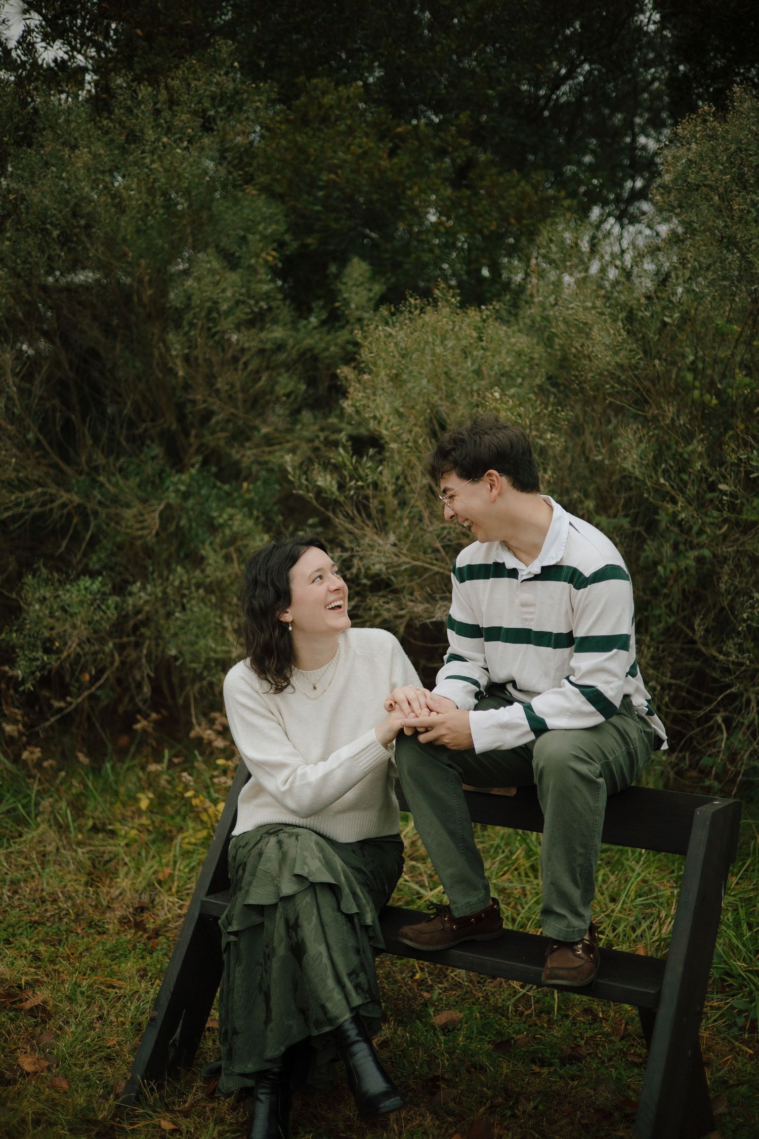 A couple shares a tender moment while sitting on a wooden bench surrounded by greenery.