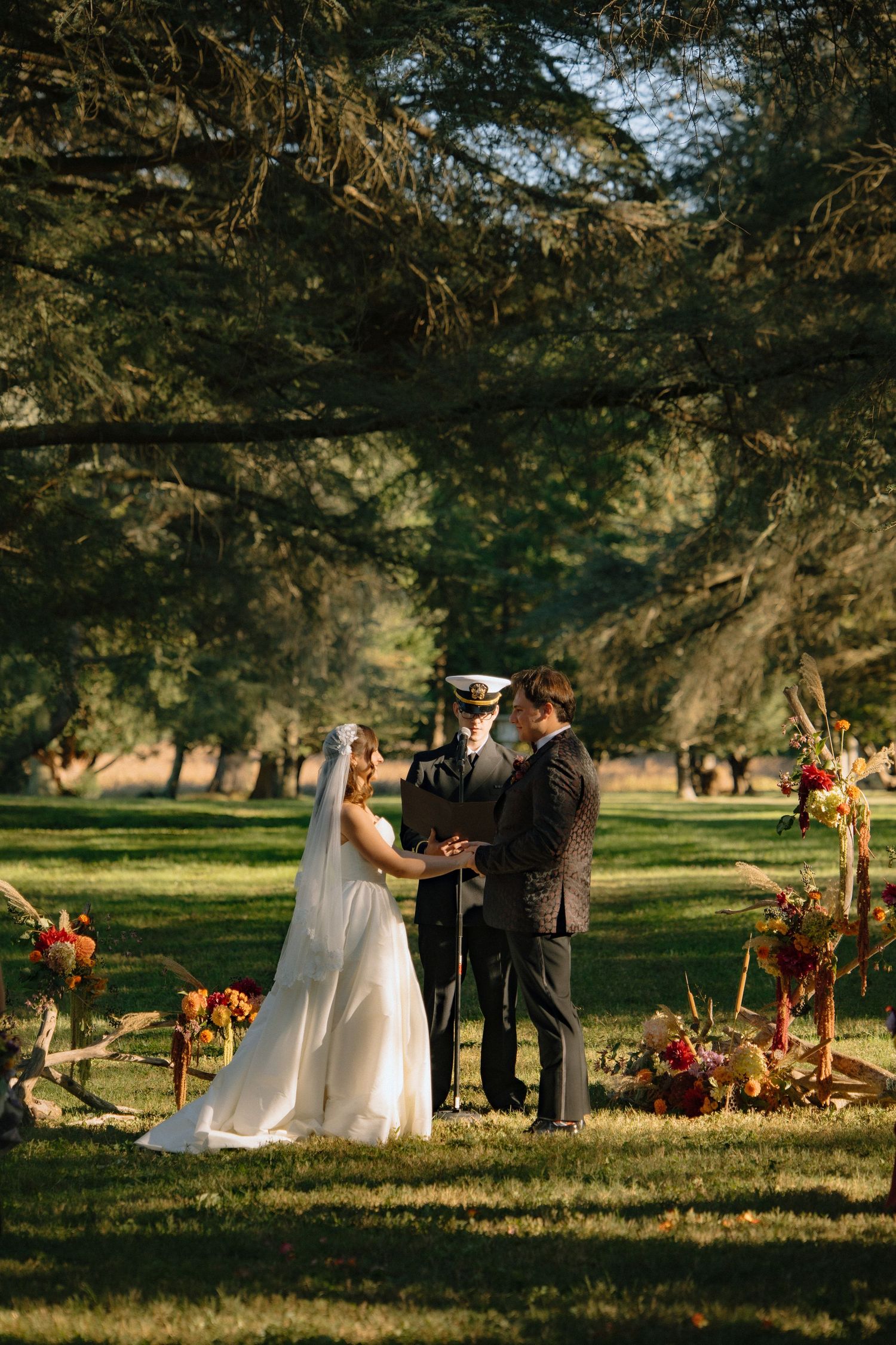 A couple shares an intimate moment in a sunlit park setting with autumn floral arrangements nearby.