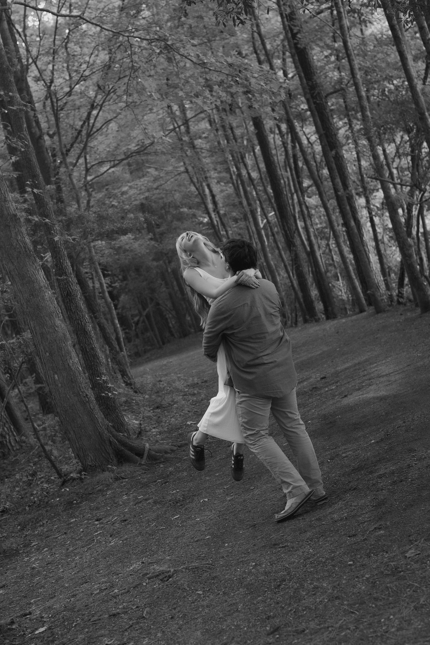 A couple dances playfully through a wooded forest path.