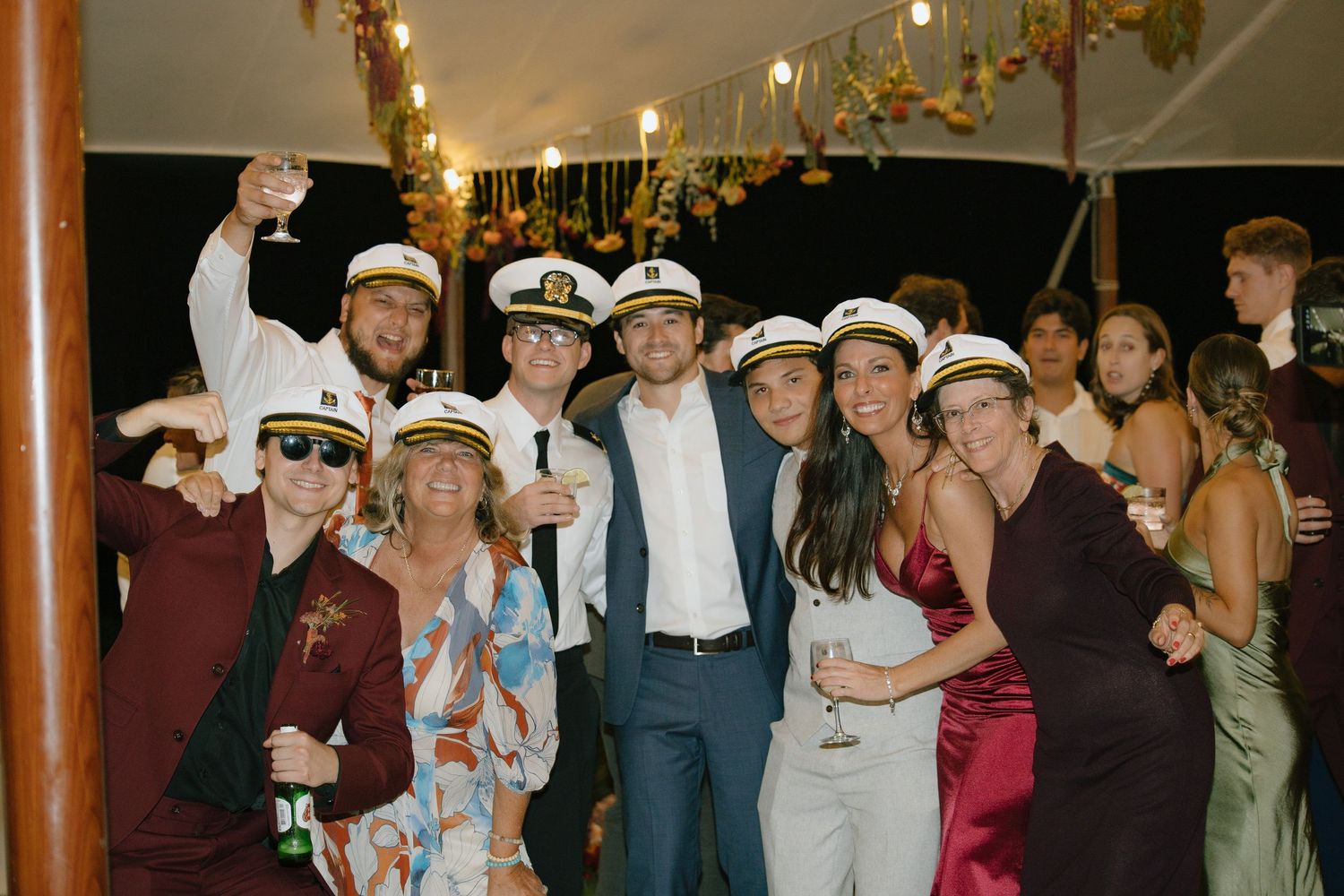 Wedding party members pose wearing nautical captain hats during evening reception celebrations.