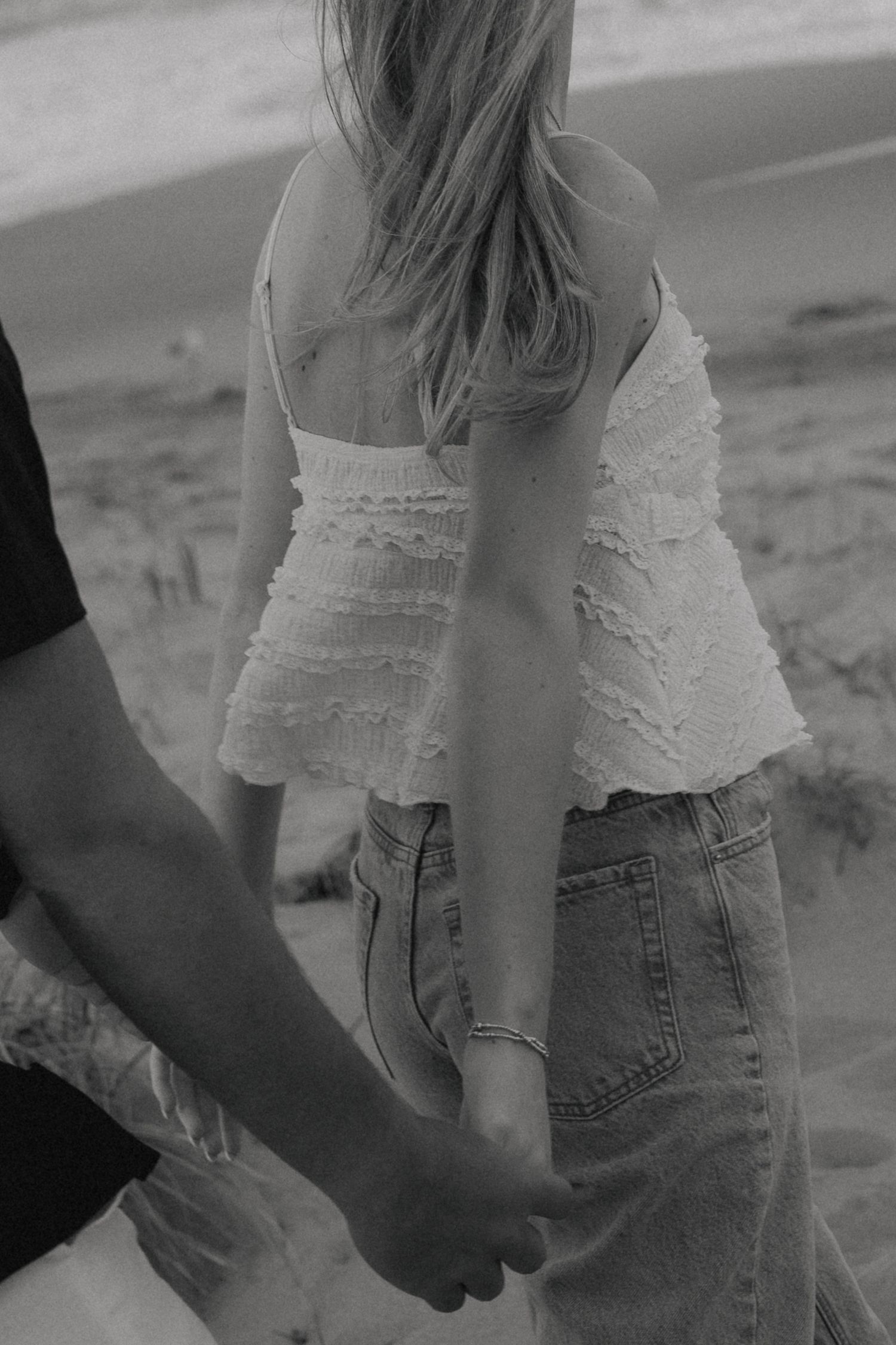 Close-up details of a white lace top and denim jeans on a beach.