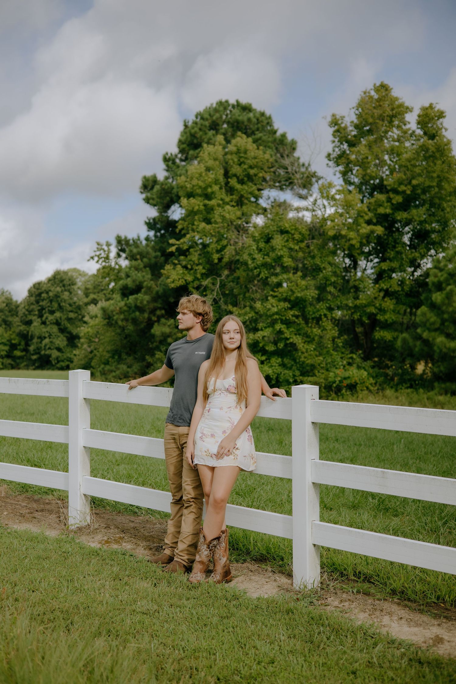 A couple walks along a white fence line on a grassy hillside.