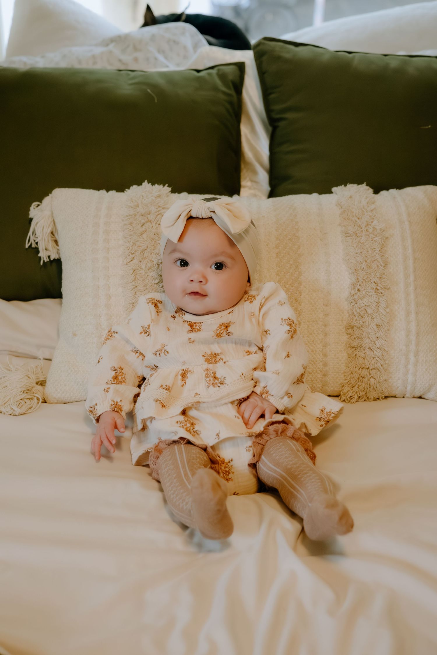 Baby wearing a delicate cream-colored lace dress lying on white bedding.
