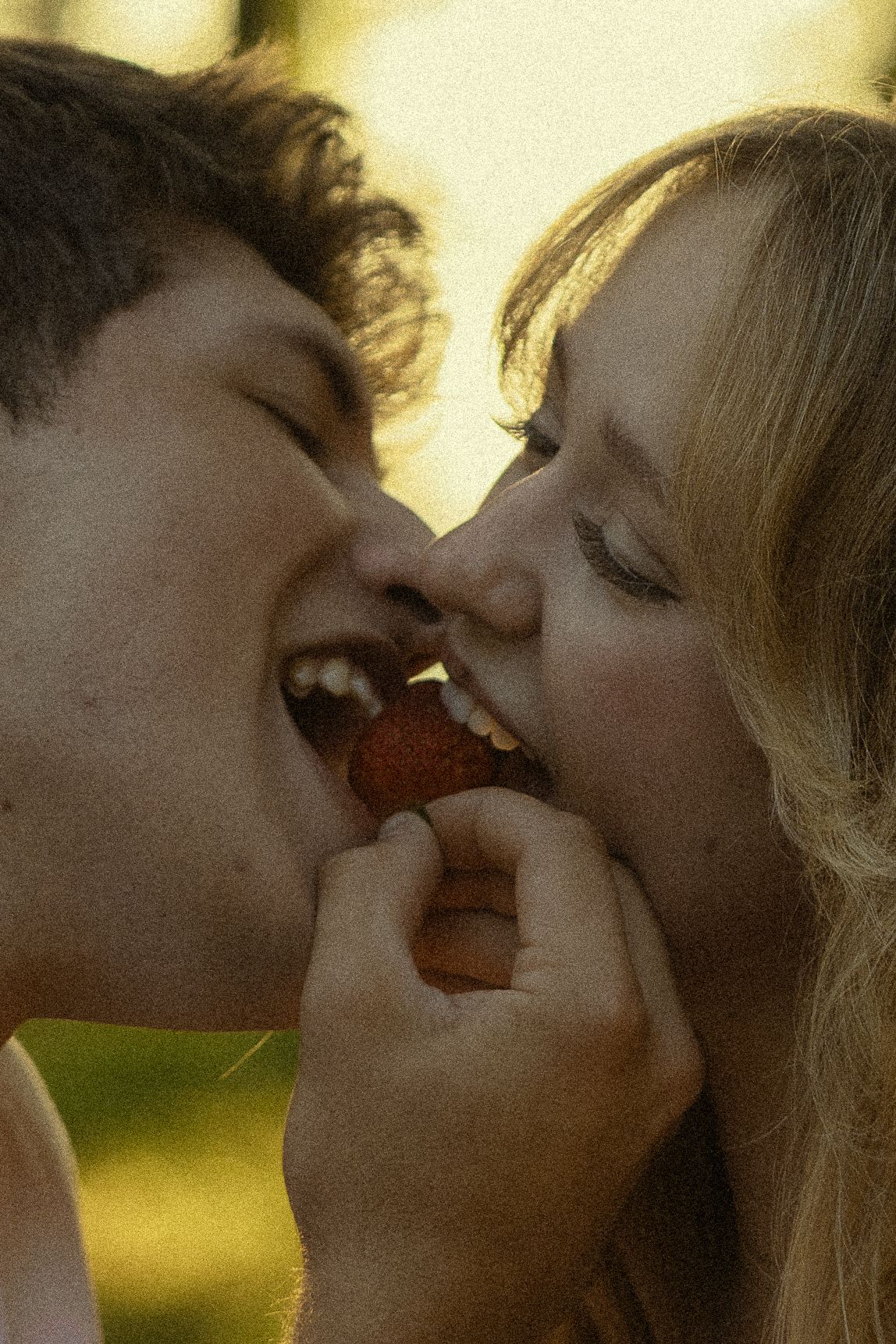 A romantic couple sharing a strawberry together outdoors in warm golden light.