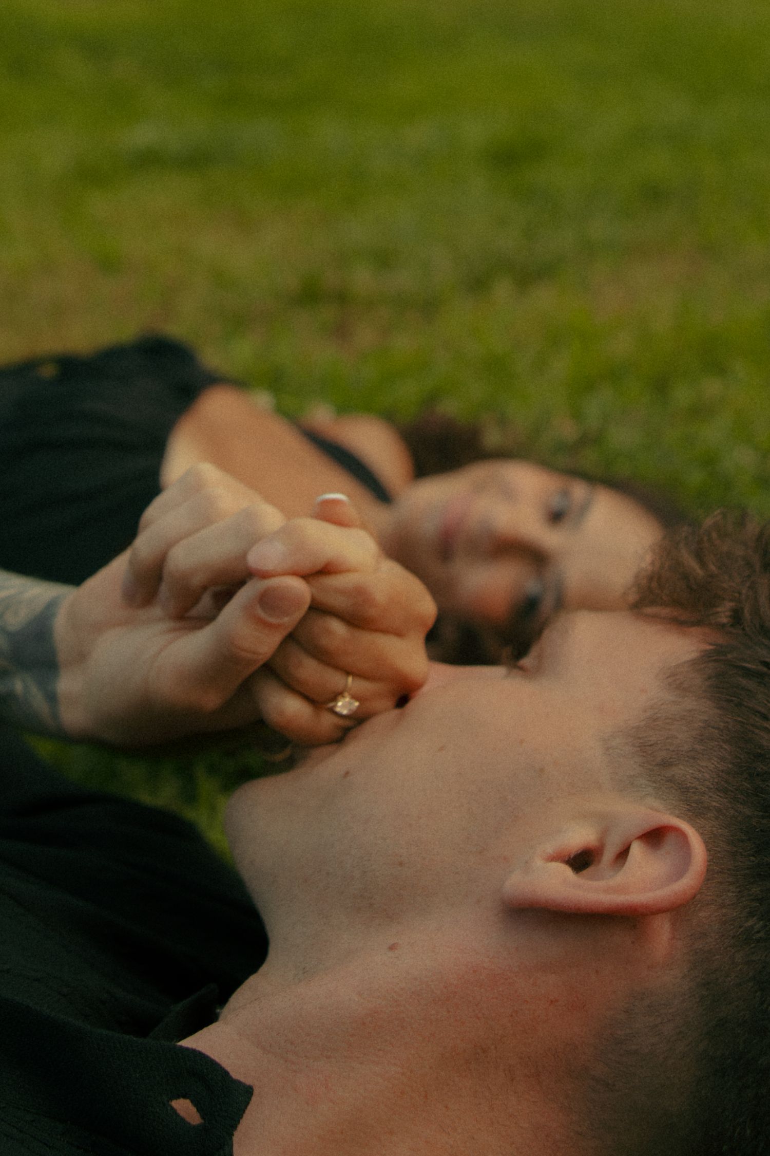 Couple lying on grass holding hands, woman wearing diamond engagement ring,  in fredricksburg, va. virginia engagement photographer