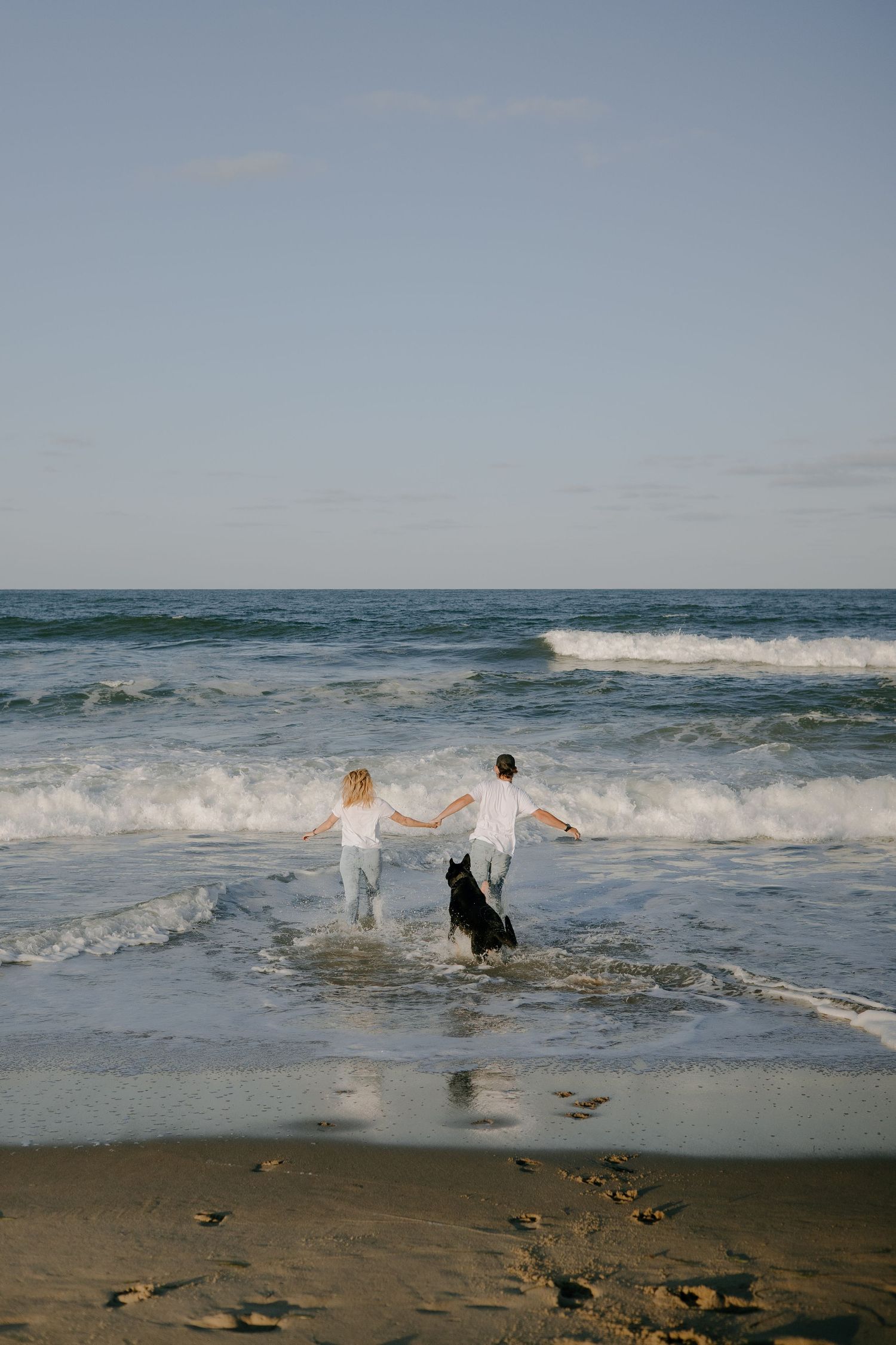 Two people running into the ocean waves together on a sunny beach day.