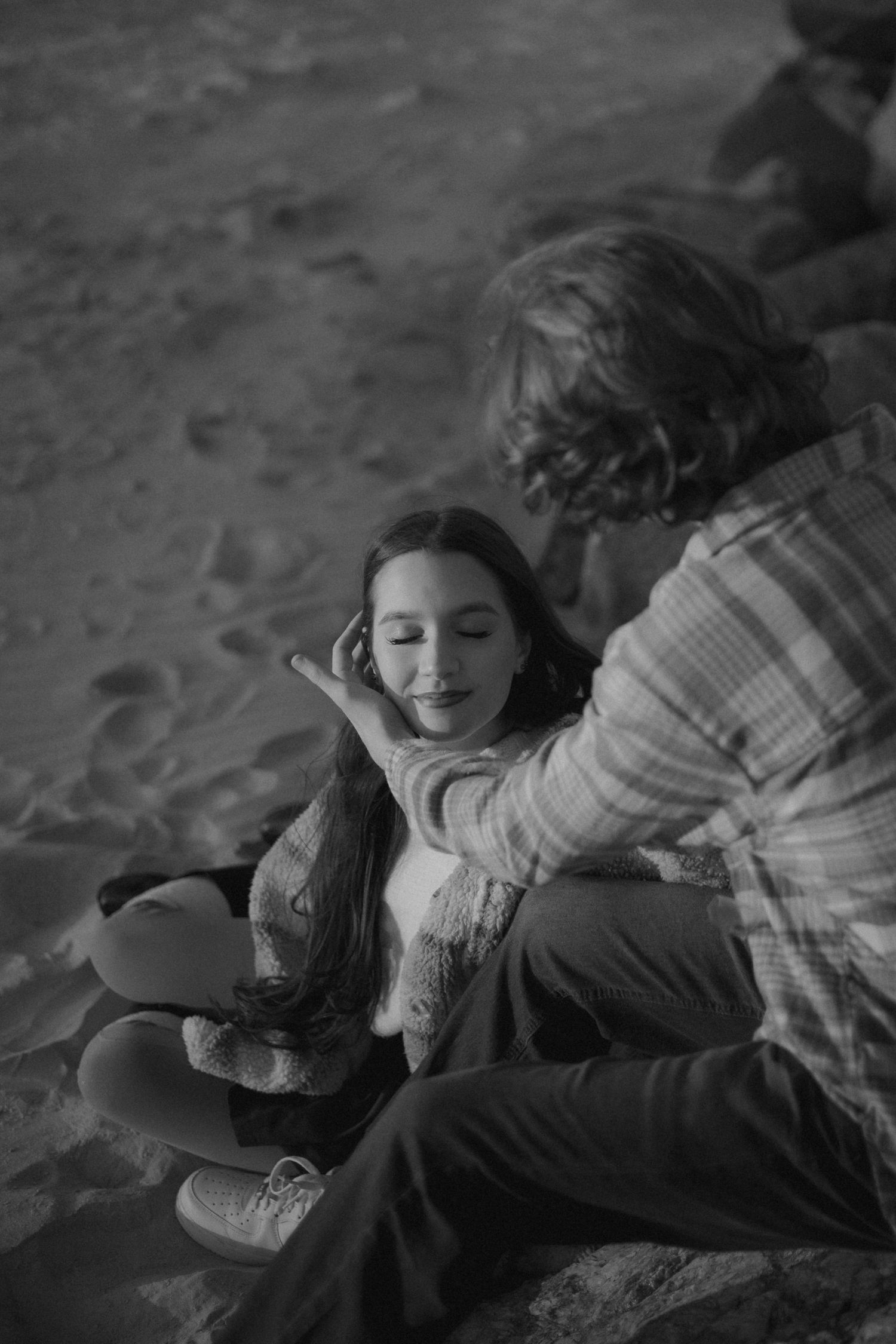 A couple lies on the beach sand sharing a joyful moment at twilight.