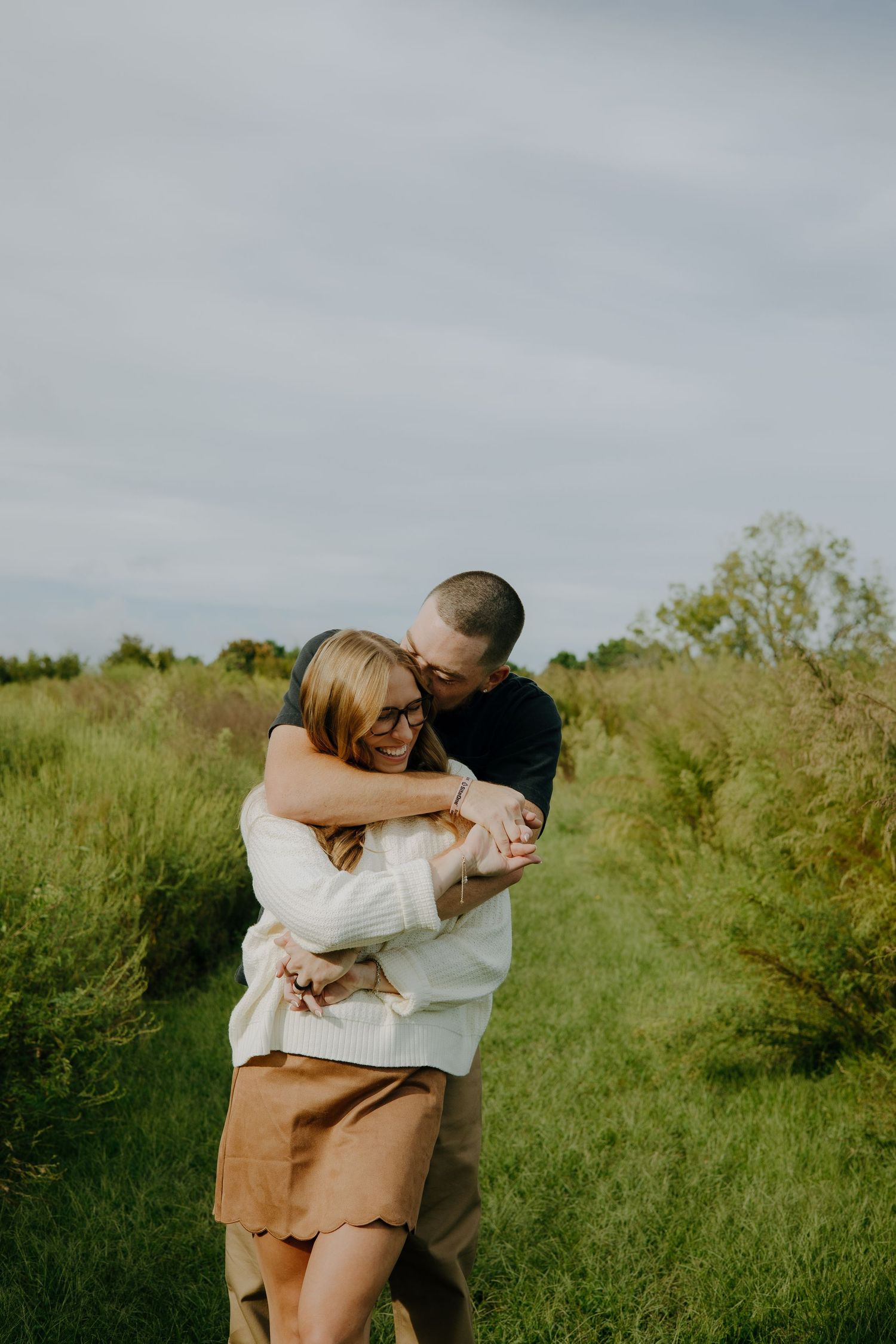 Couple embracing in a sunny meadow with tall grass and soft lighting.