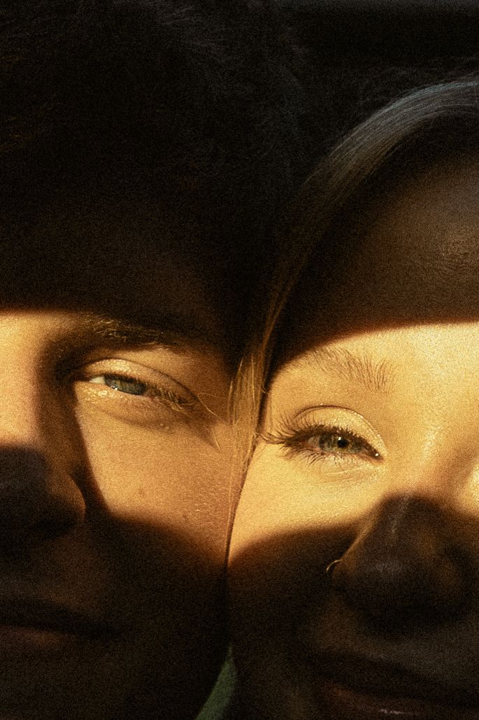 Two faces bathed in warm golden light and shadow, eyes visible, creating a dramatic and intimate portrait.