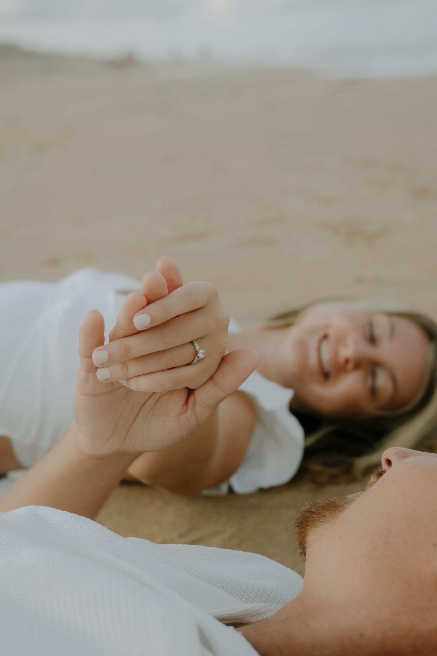 A couple lying down and holding hands intimately against a light background.