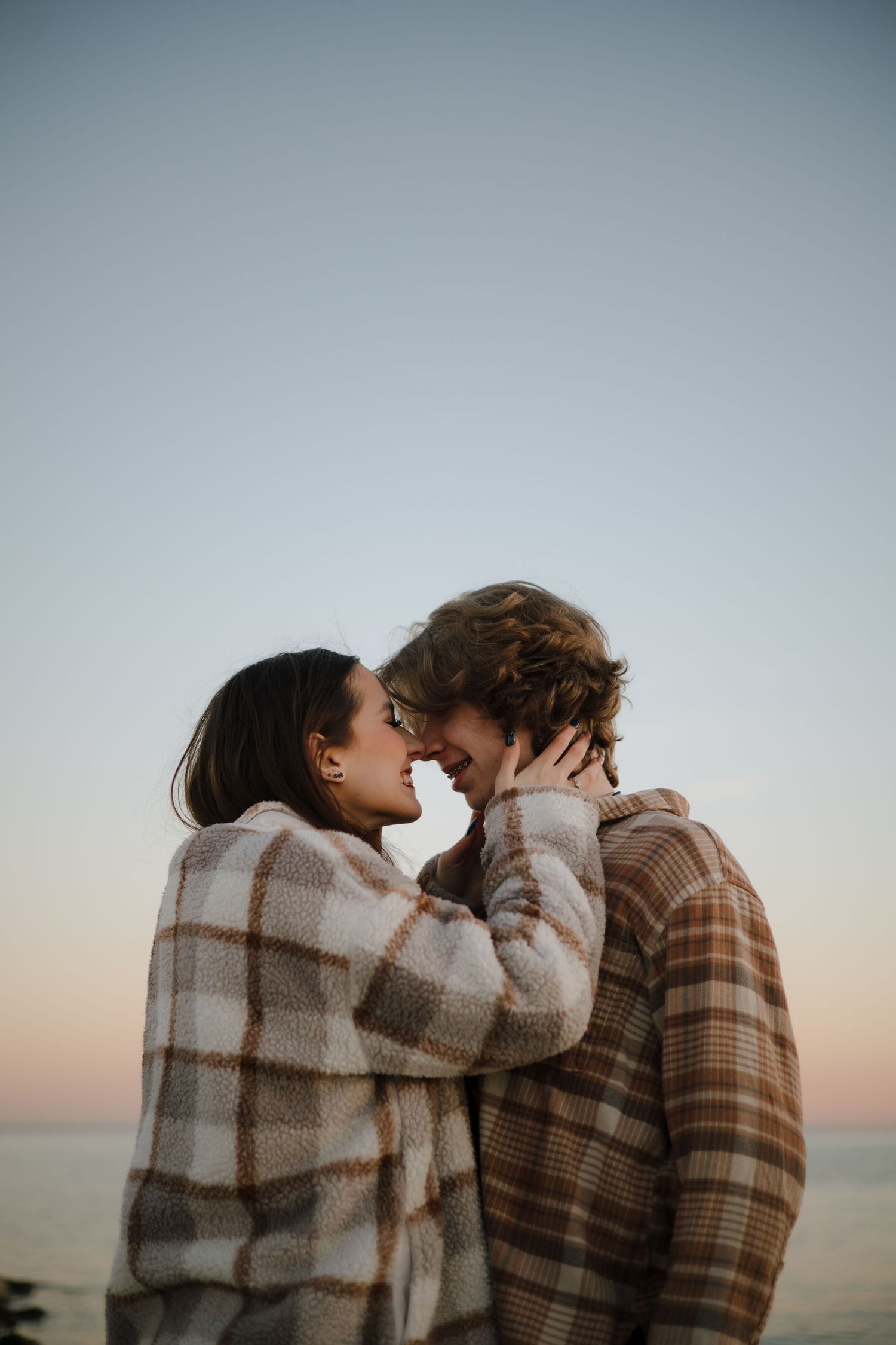 Two people share a tender moment against a sunset sky backdrop.