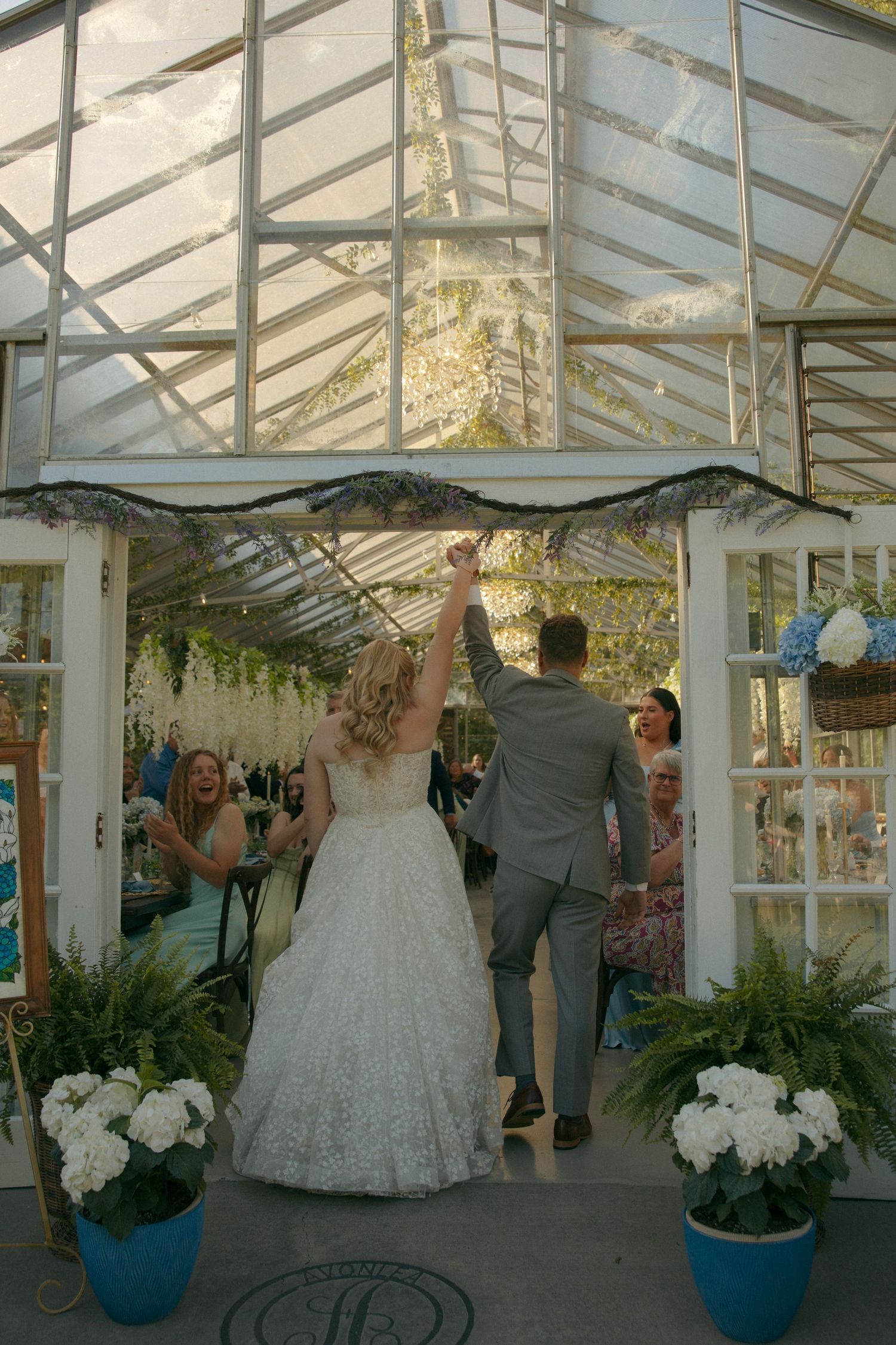 Bride and groom entering greenhouse wedding reception with raised hands at at Avonlea Farms in Mineral, VA.