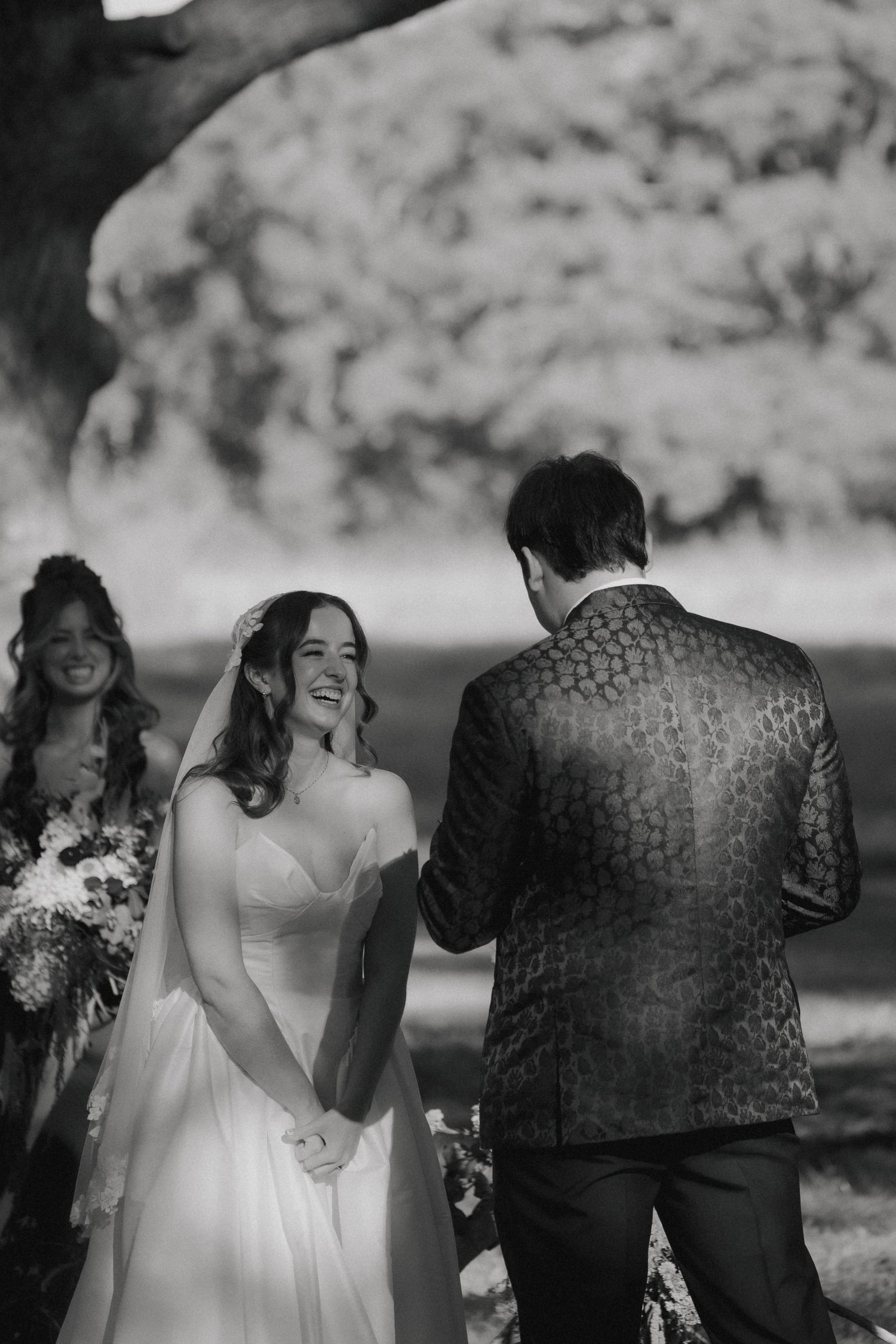 A black and white photo series shows a couple and wedding party laughing together outdoors during a candid moment.