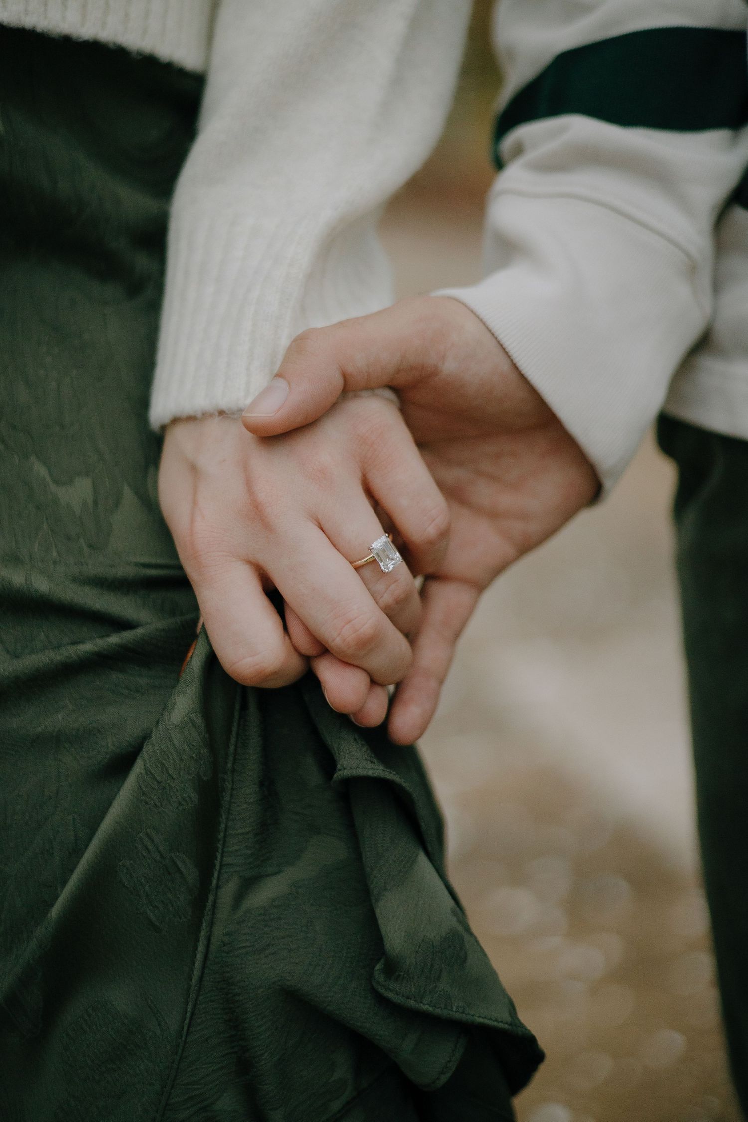 Close-up of intertwined hands with an engagement ring against cozy sweater fabric.