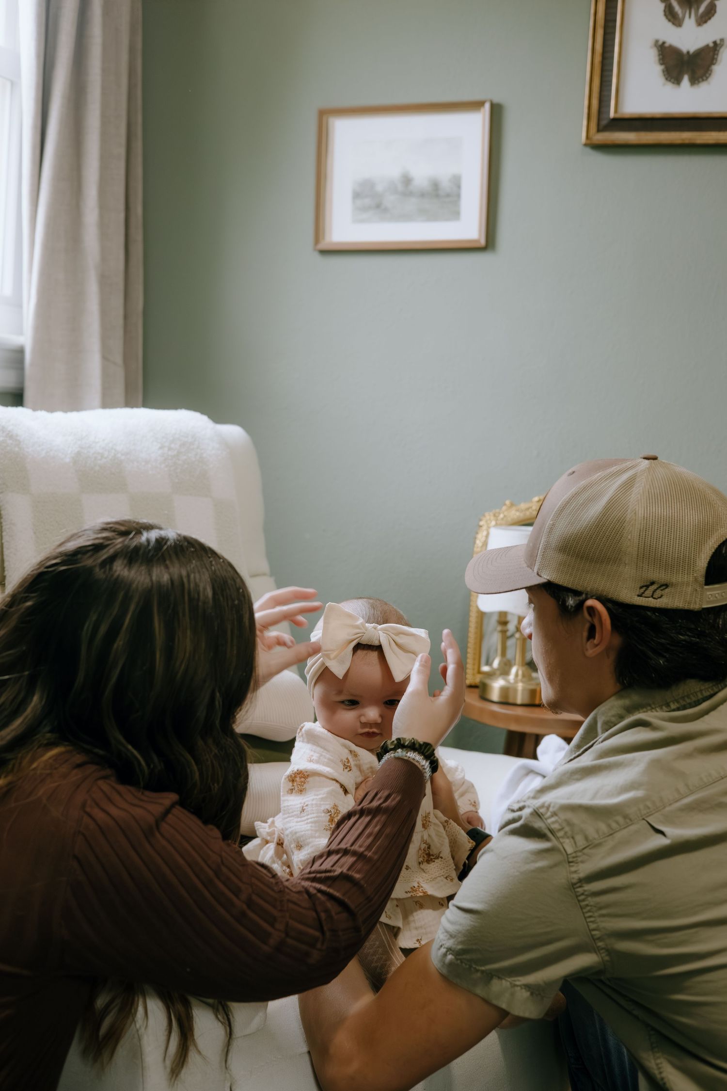 A sweet moment of play between a baby in a white dress and adults in a cozy living room setting.