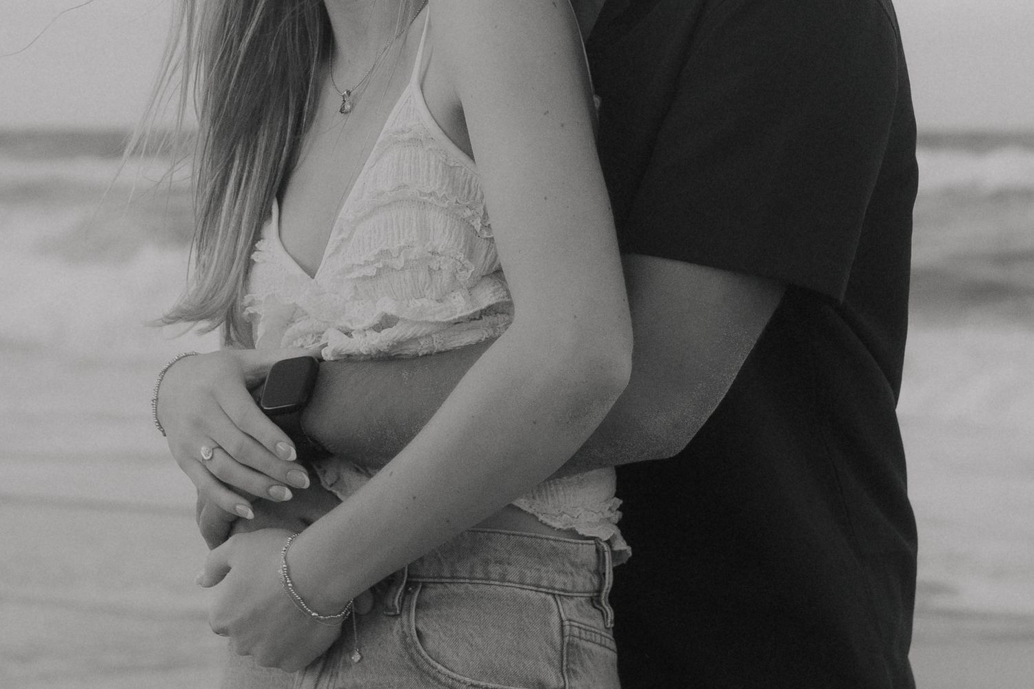A romantic black and white photo showing a couple embracing on a beach, with focus on their intertwined arms.