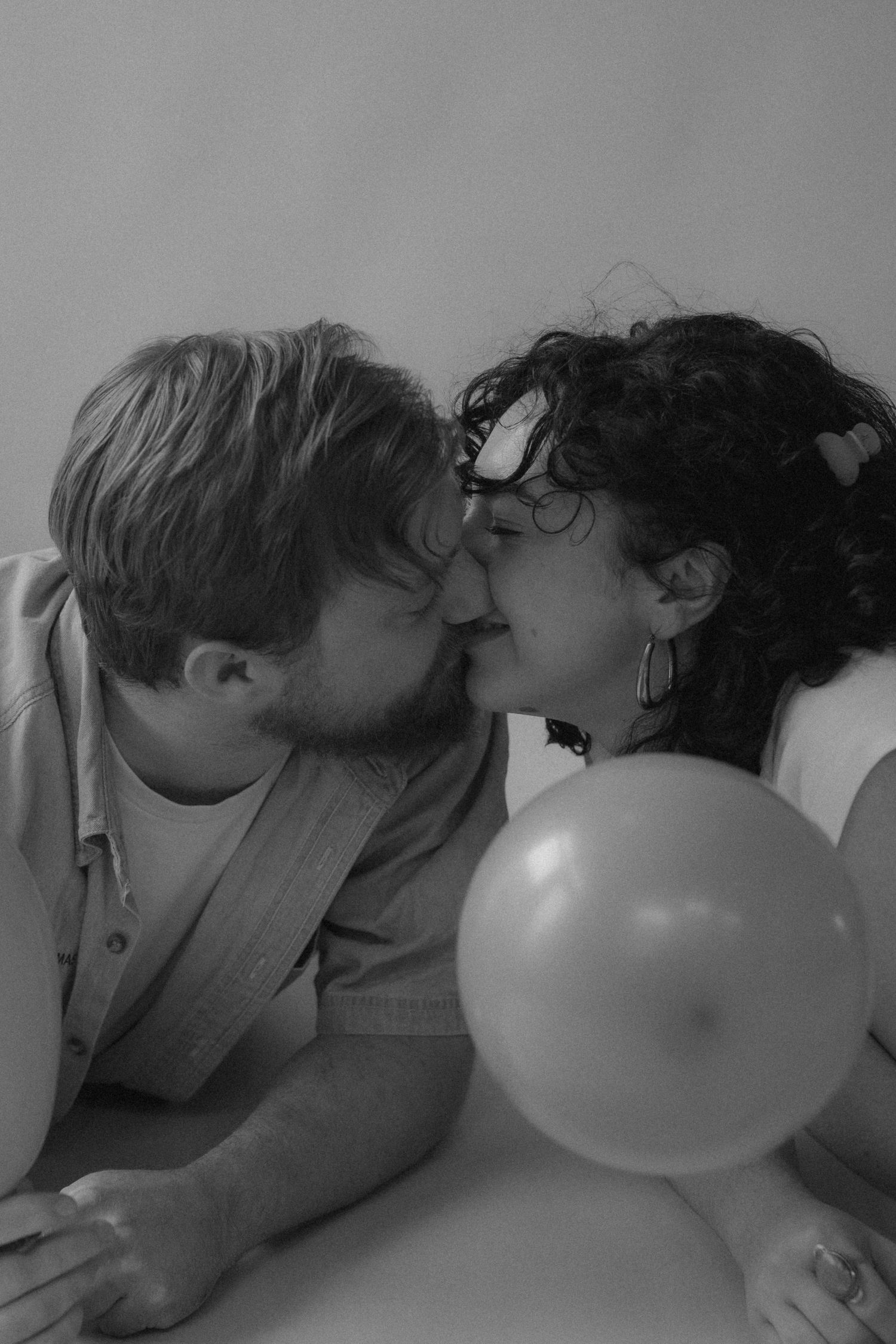 A romantic black and white photo of a couple sharing an intimate moment with a balloon in the foreground.