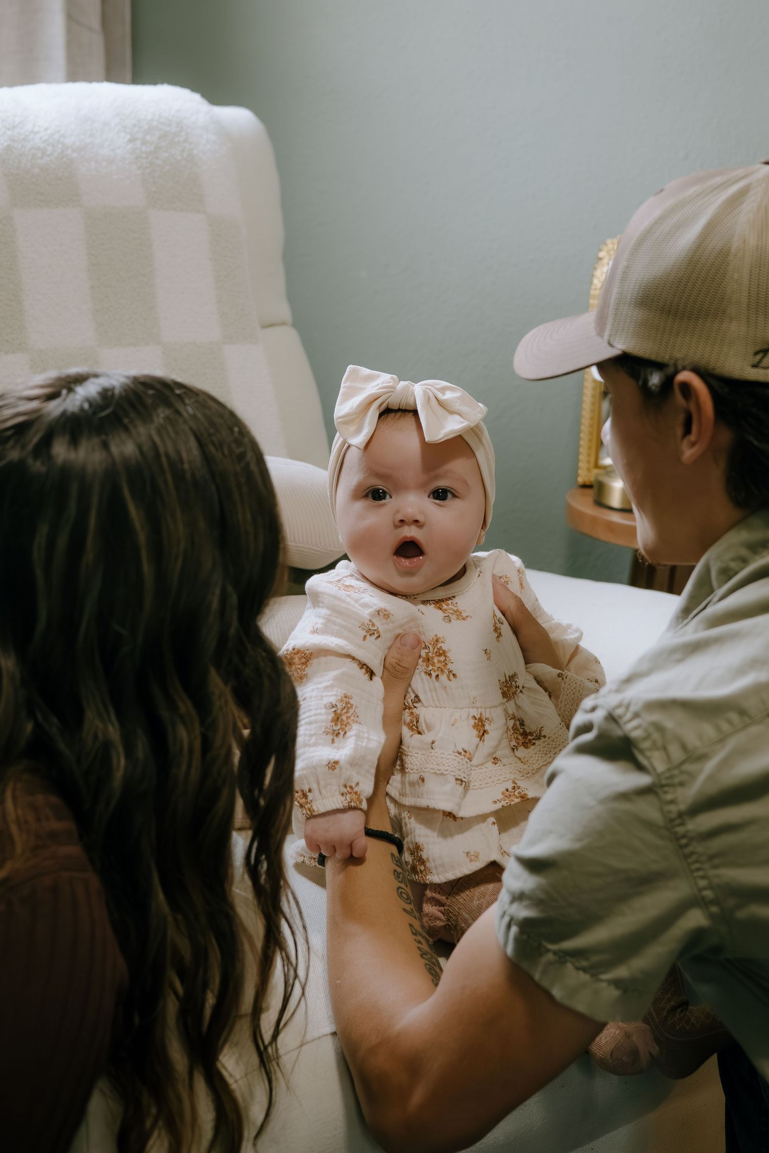 Baby in a floral dress and white bow being lifted up during playtime.