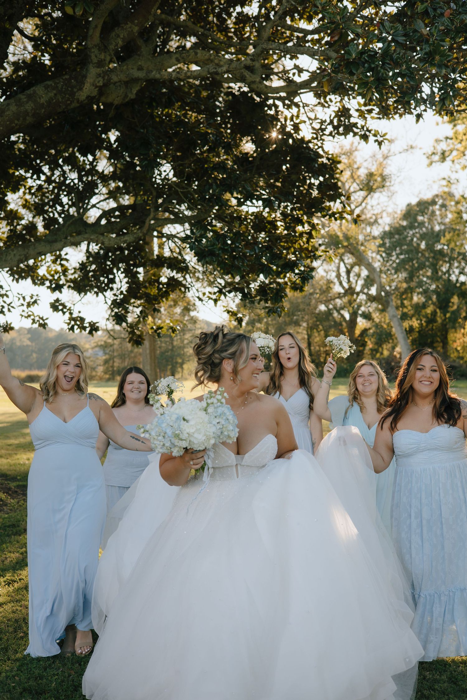 Bridesmaids in light blue dresses laughing together outdoors.