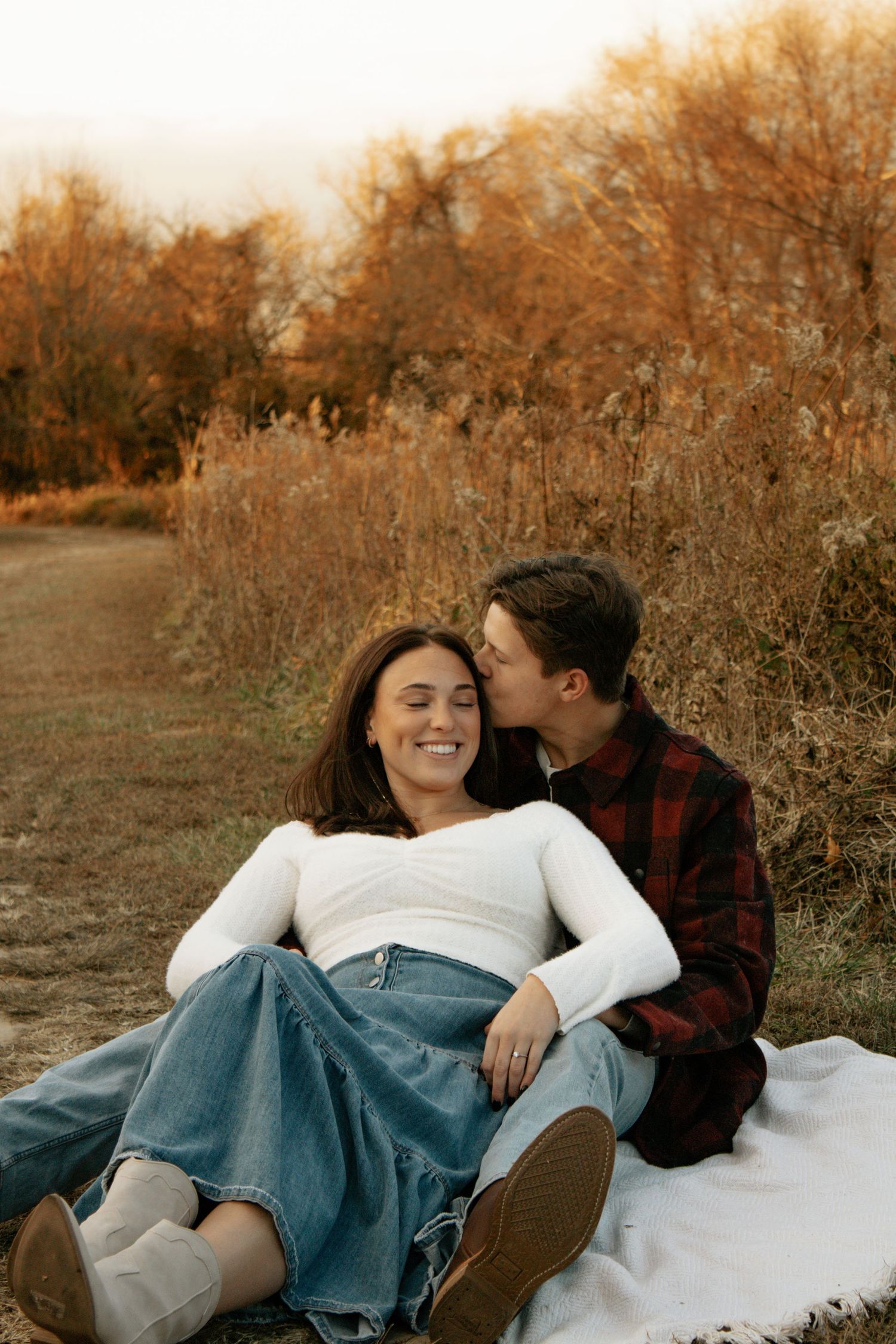 Couple lying on blanket in autumn field during golden hour.