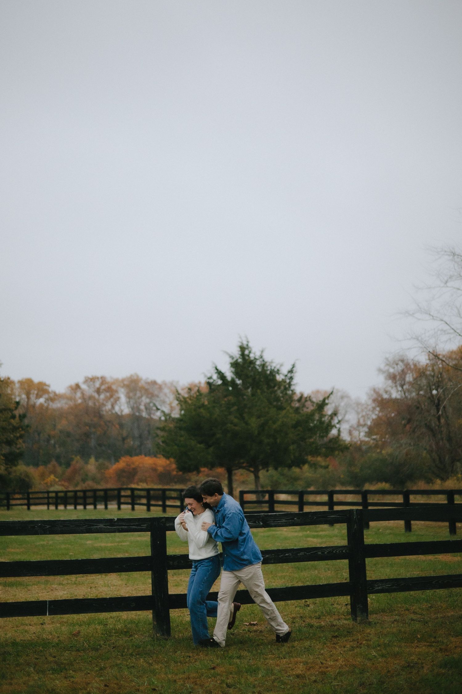 A couple walking together along a wooden fence in a pastoral autumn setting.