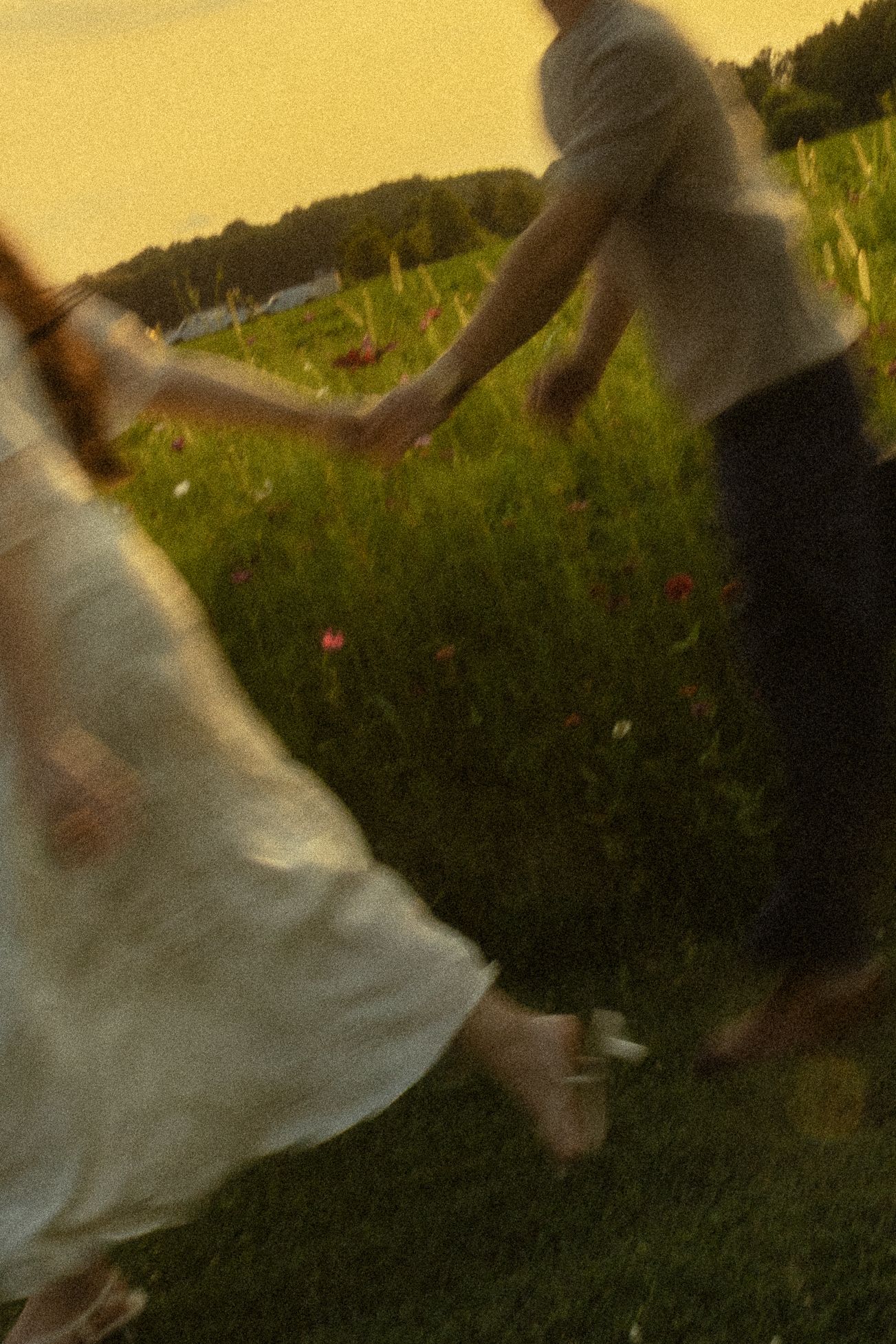 Blurry motion shot of couple holding hands running through a wildflower meadow at golden sunset.