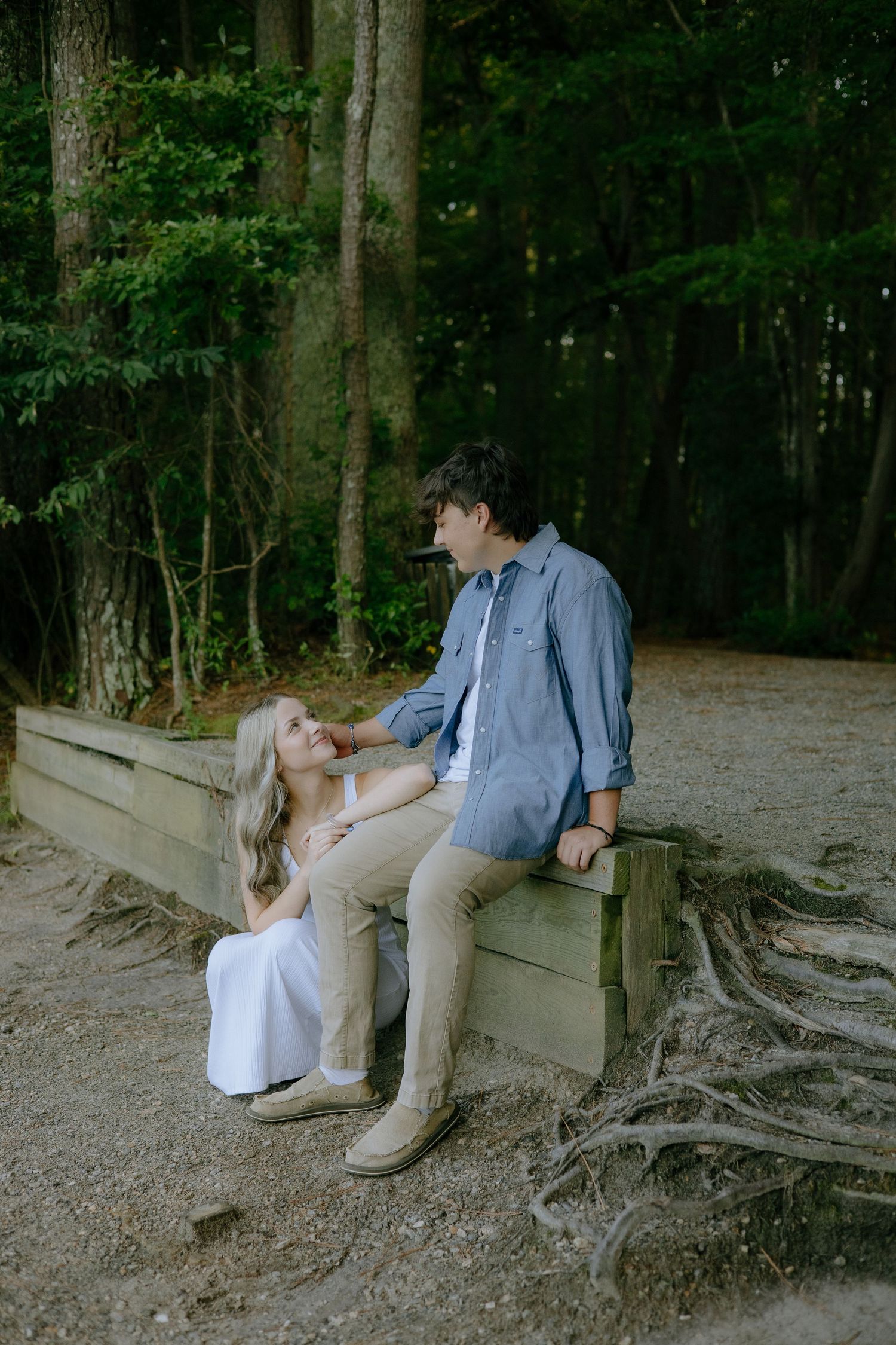A couple sits intimately on a wooden bench surrounded by a forest.