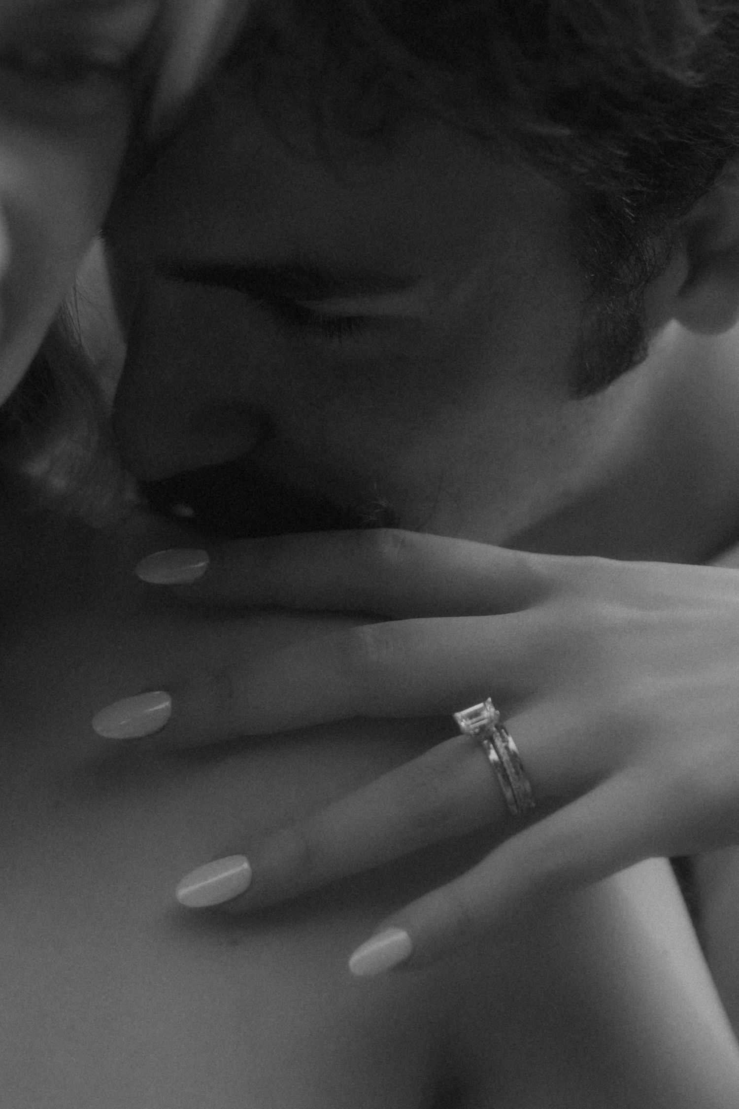 Black and white photo of a couple in an intimate moment, woman's hand showing a diamond engagement ring.