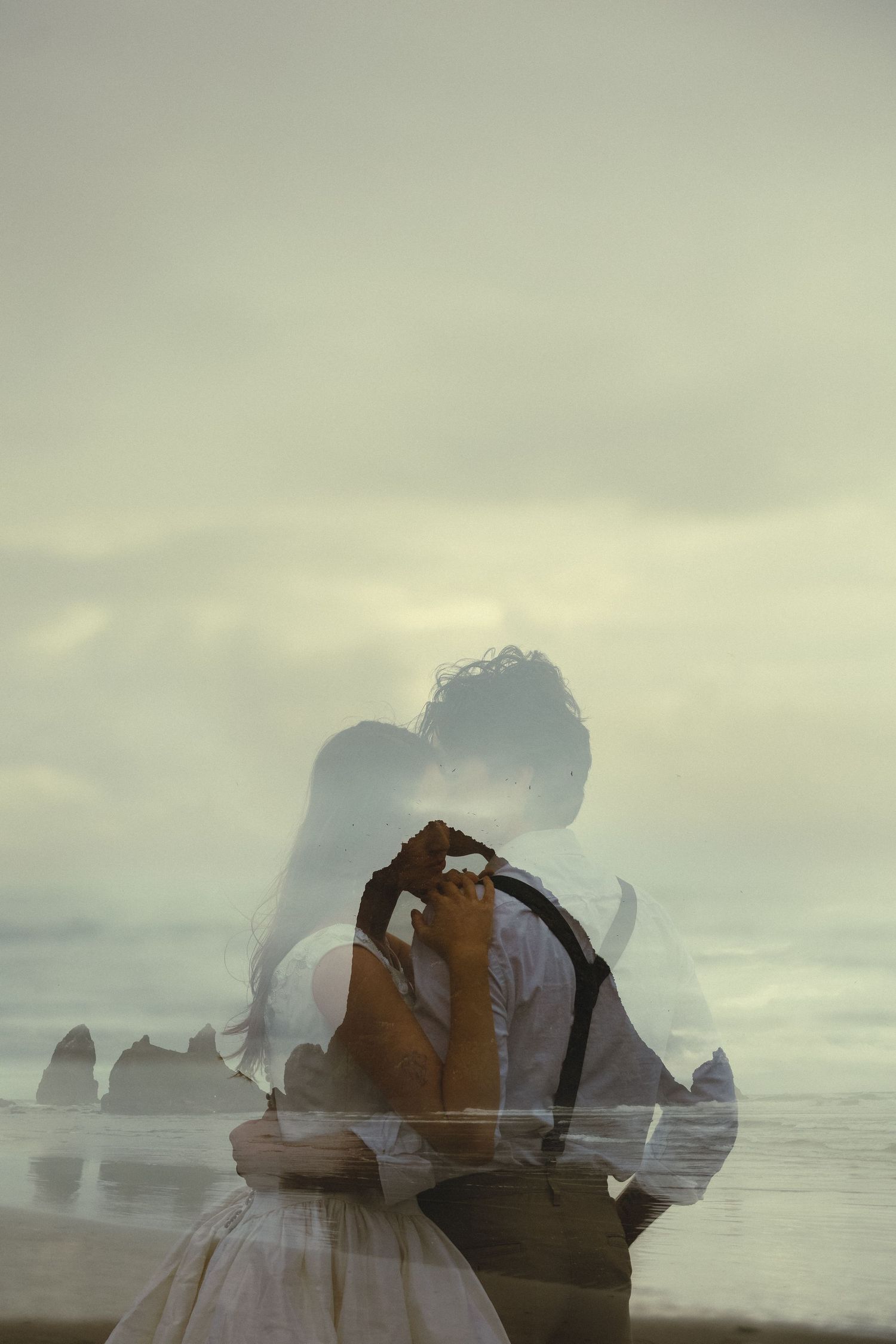 Double exposure photo of a couple embracing and kissing on a misty beach with rocky sea stacks.
