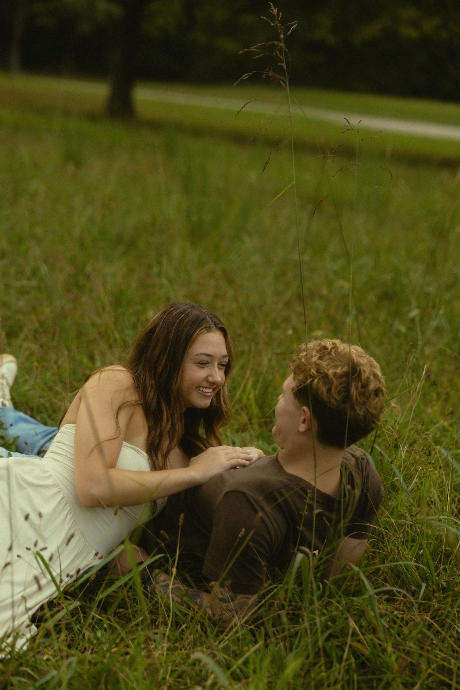 A young couple smiling and lying together in a lush green meadow on a warm summer day.