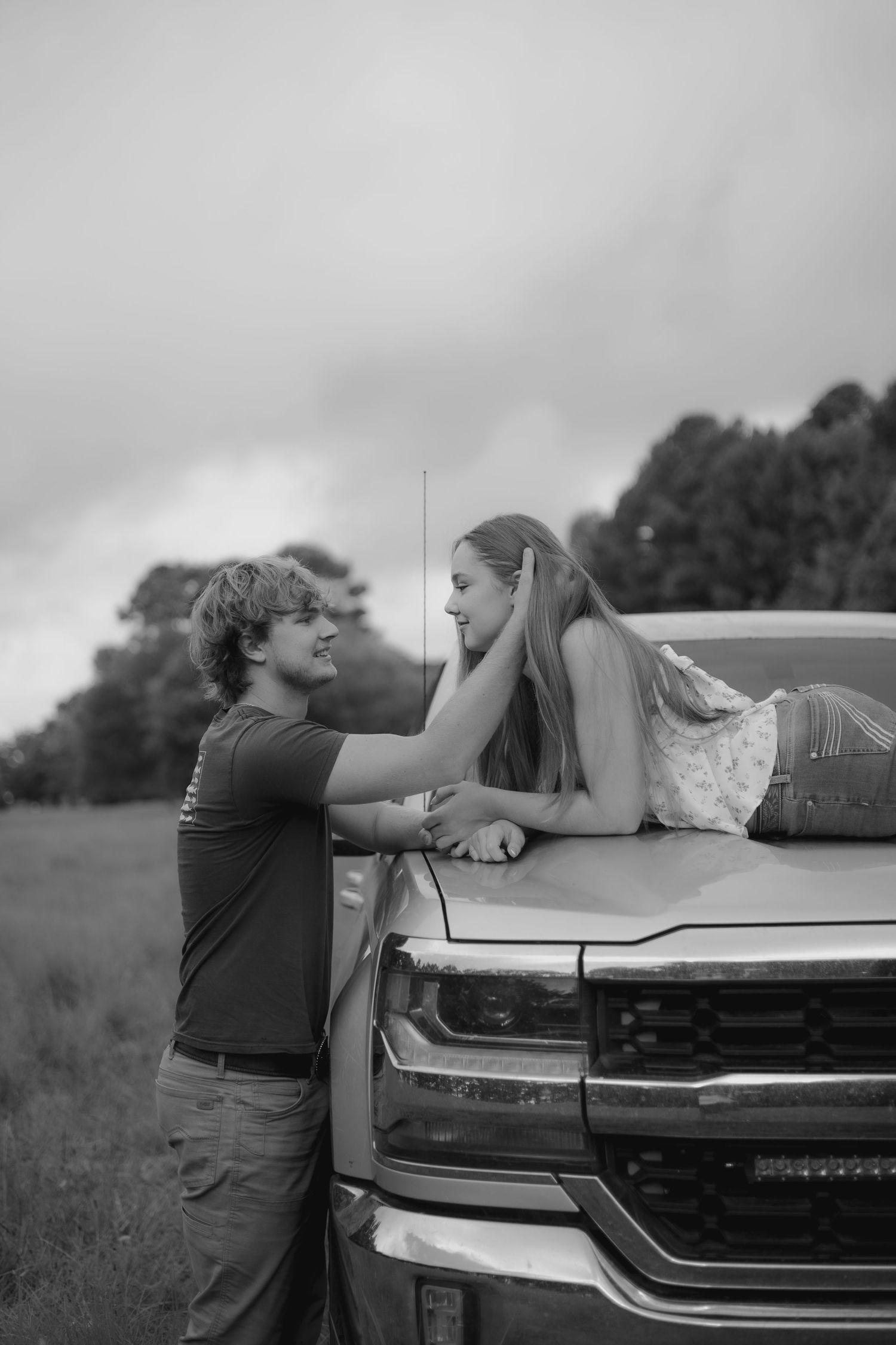 A tender moment shared between a couple leaning against a truck's hood.