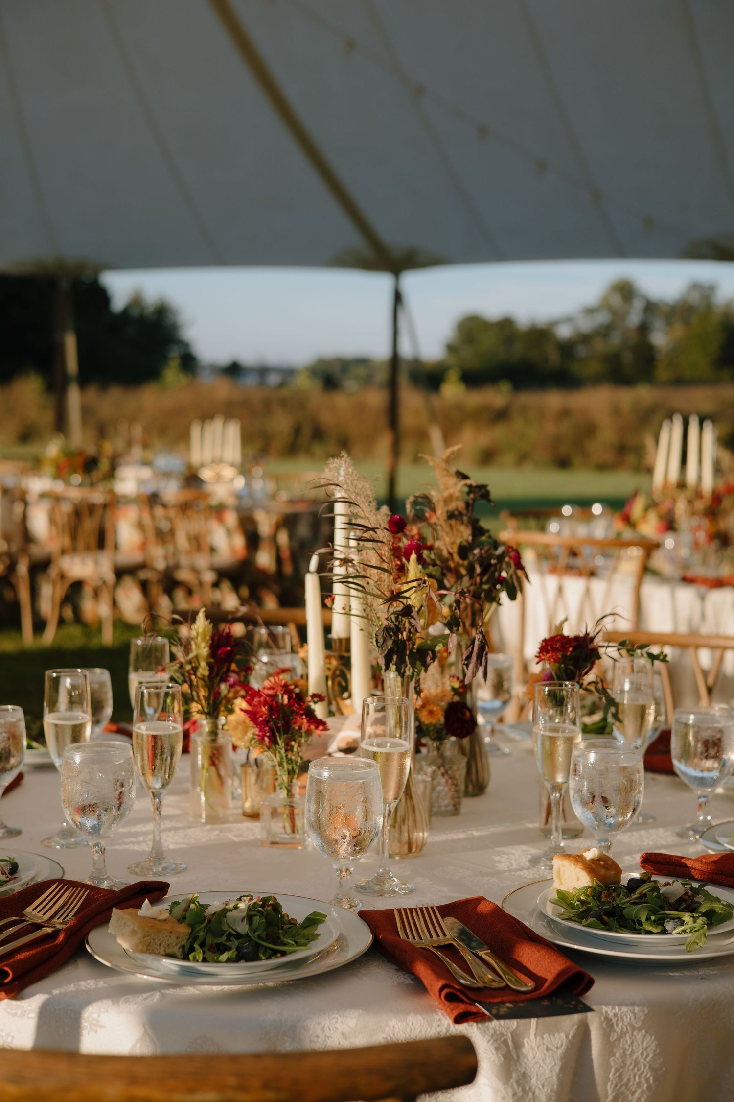 An elegant wedding reception table setting with floral centerpieces and glowing candlelight under a tent.