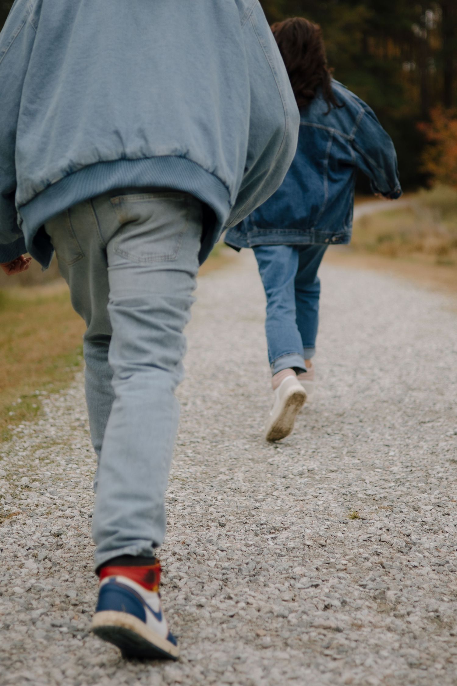 Close-up view of feet walking on a gravel path wearing sneakers and casual clothing.