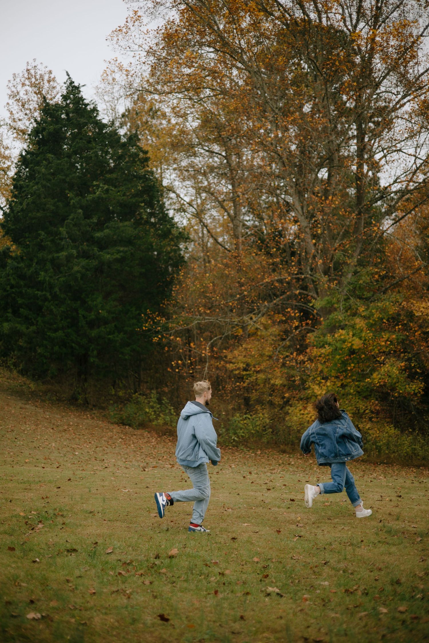 People running and playing on a grassy hillside surrounded by fall foliage.