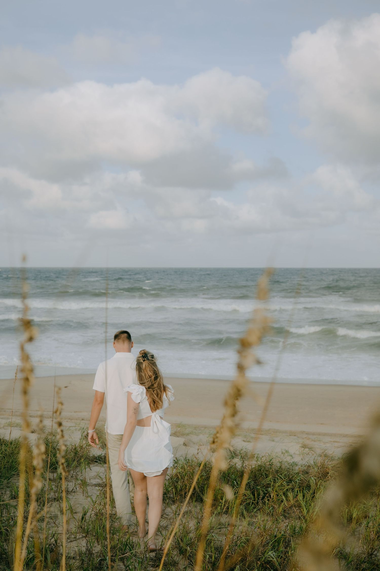 A couple stands on a beach path overlooking the ocean through golden sea grass.