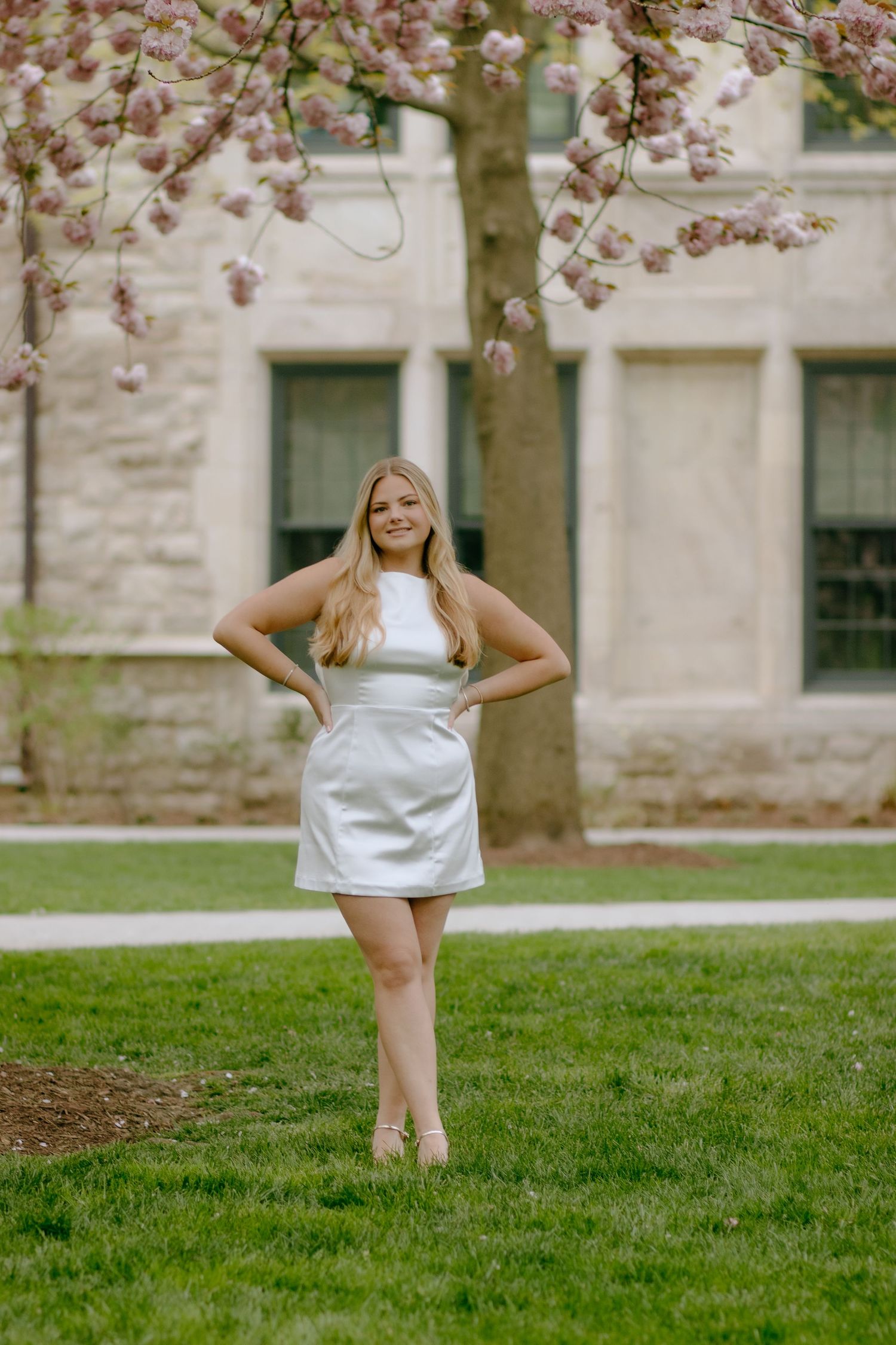 A playful photoshoot on a grassy lawn in front of a stone building with cherry blossoms overhead.