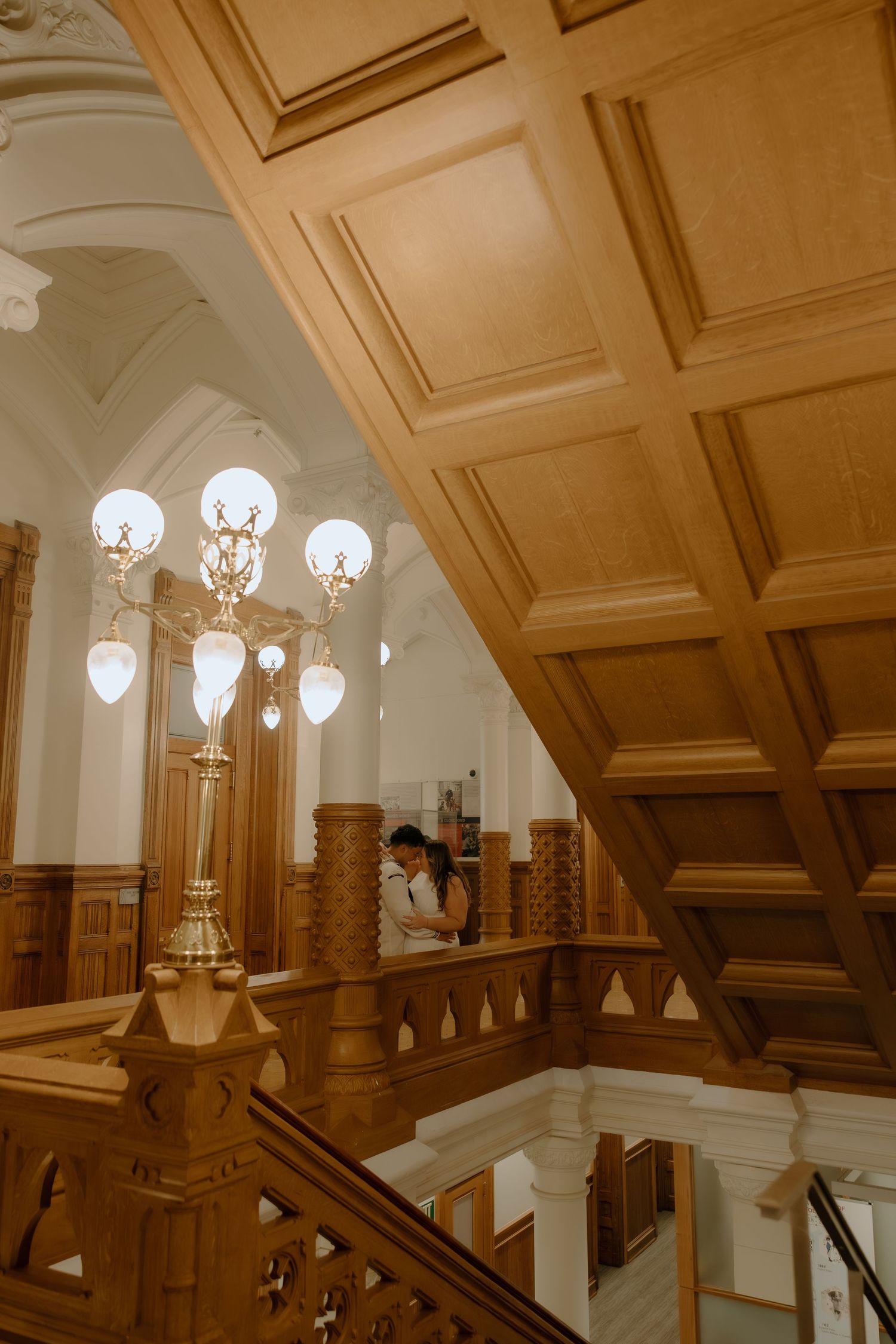 Elegant wooden staircase with ornate chandelier in a grand historic building interior.
