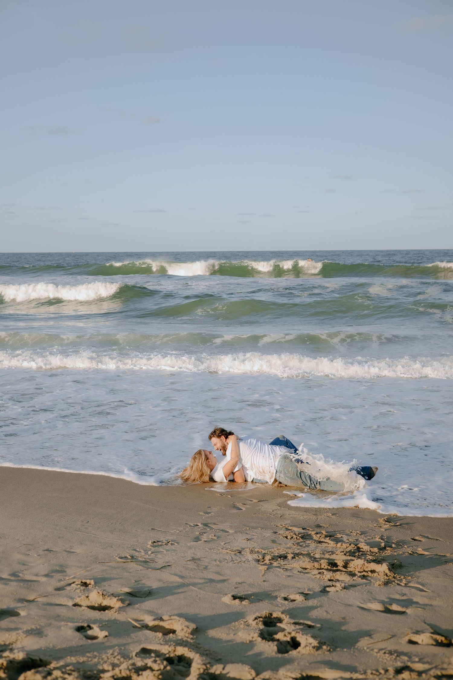 Two people lay on the beach sand as ocean waves crash nearby.