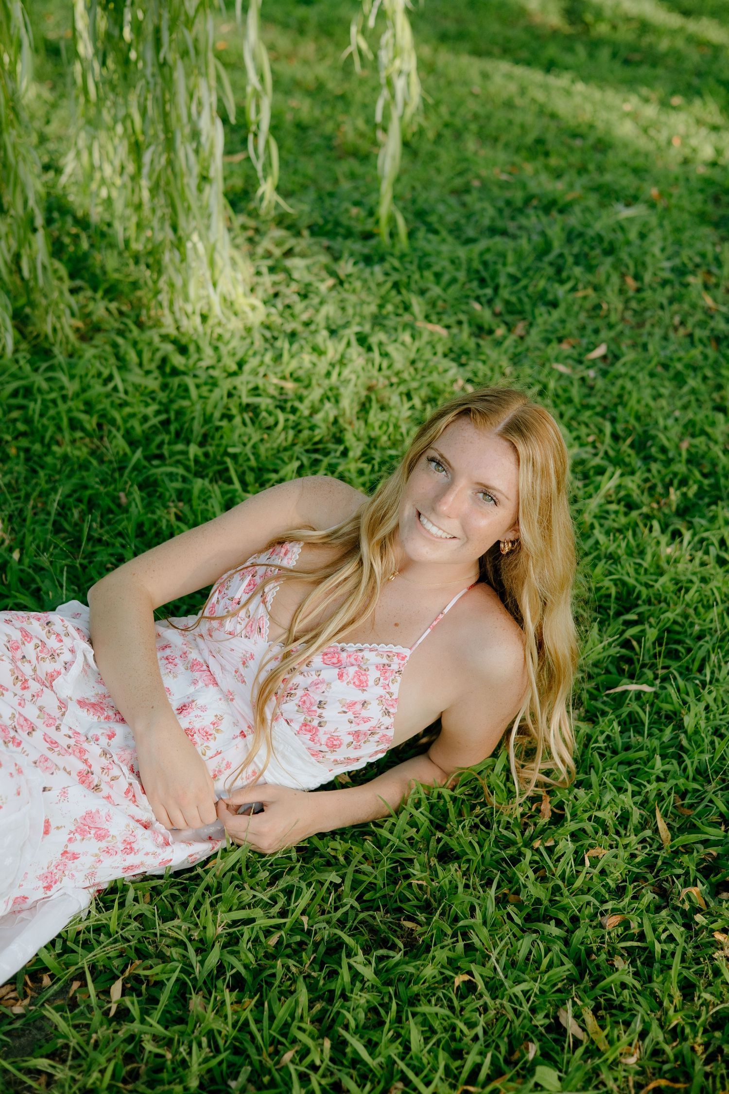 A person in a floral summer dress lying on lush green grass in a relaxed outdoor setting.