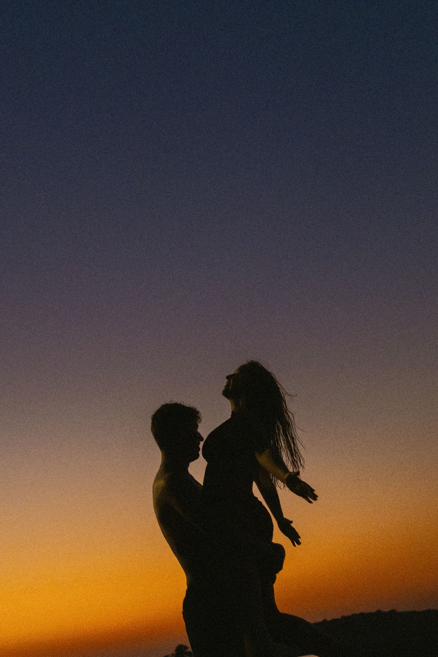 Romantic silhouette of a couple embracing at sunset with vibrant orange and blue gradient sky backdrop.