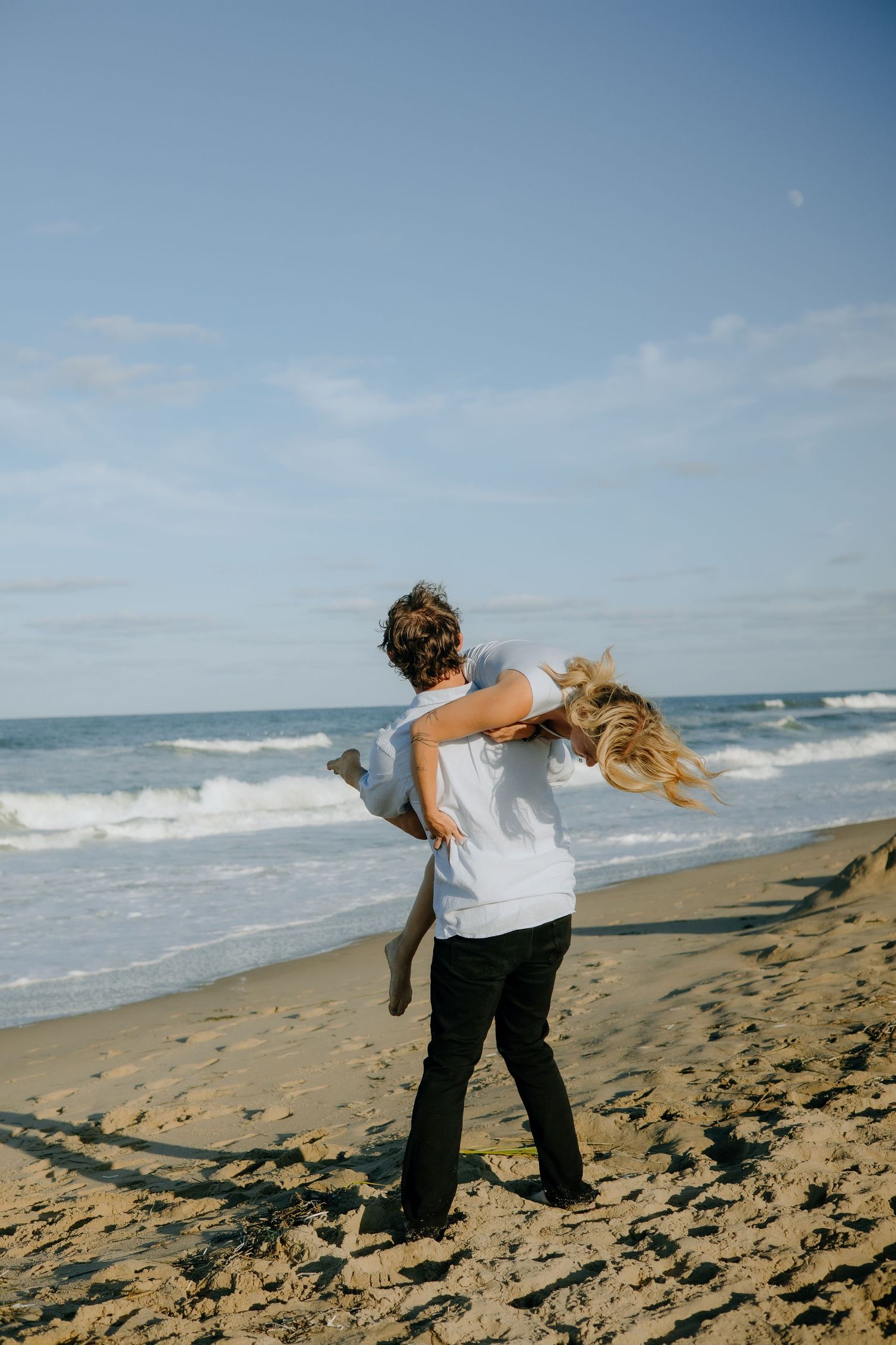 A playful couple enjoys a sunny day at the beach, running and playing in the sand.