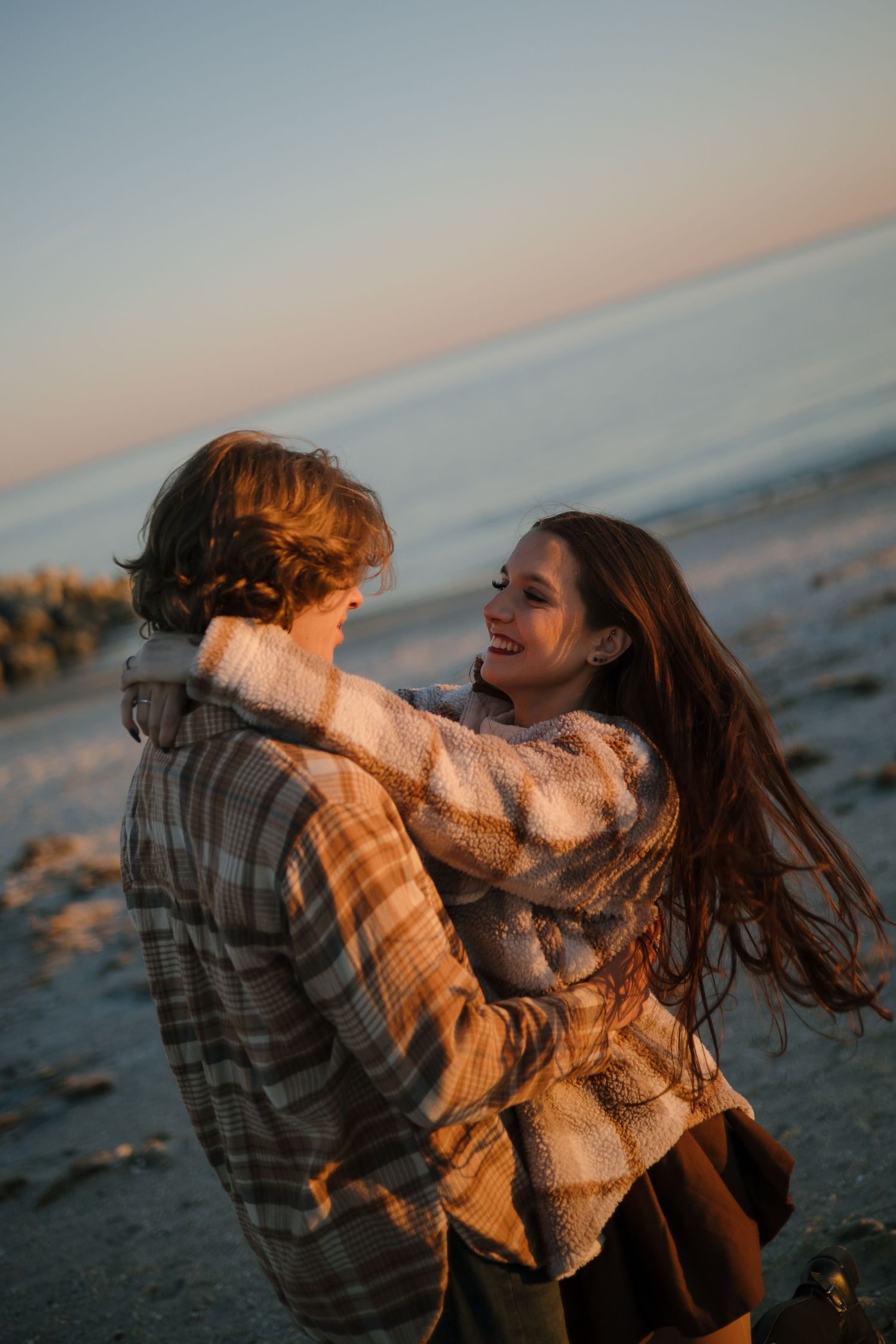 Two people share a playful moment on the beach during golden hour.