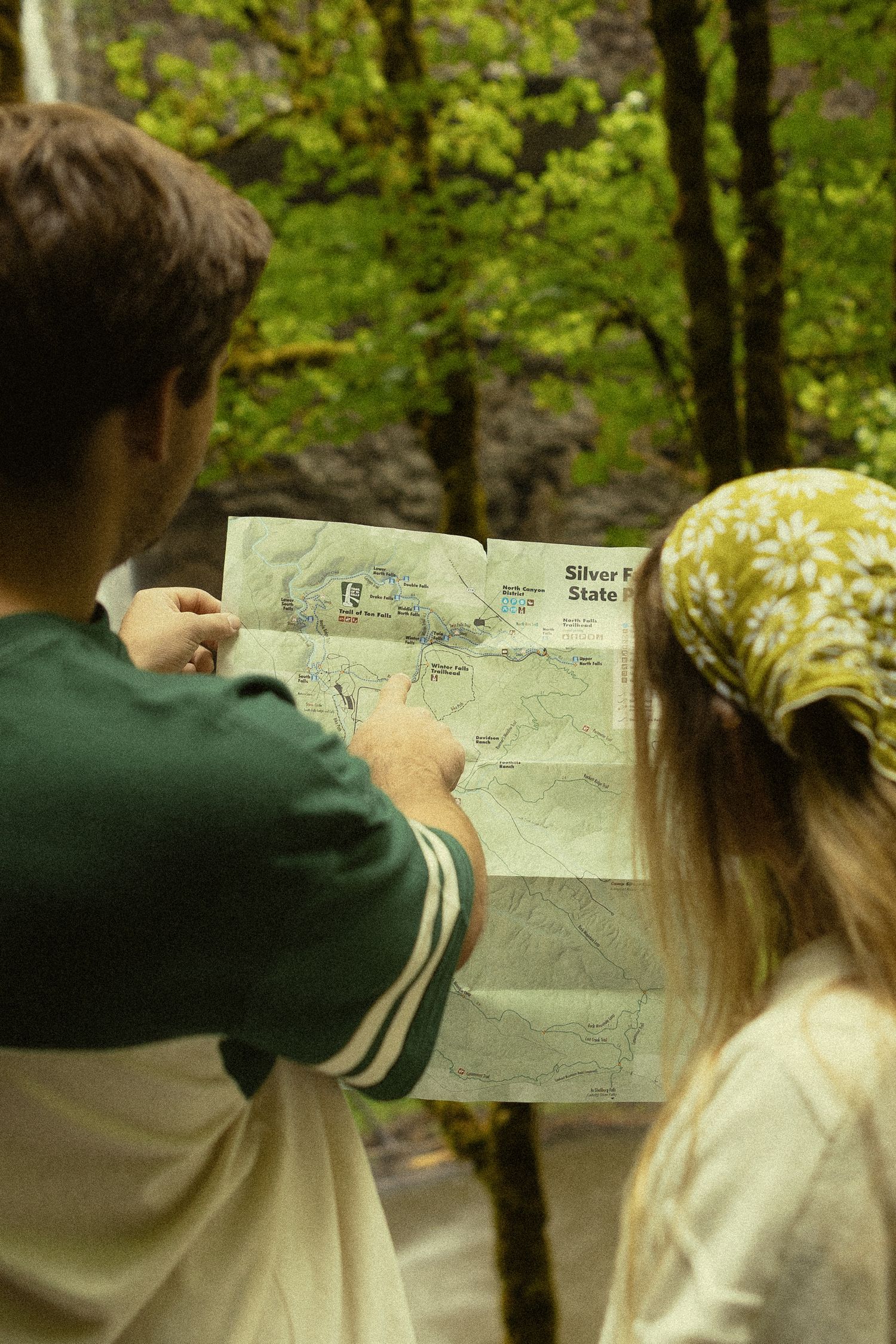 Two hikers studying a Silver Falls State Park trail map in a lush forest setting.