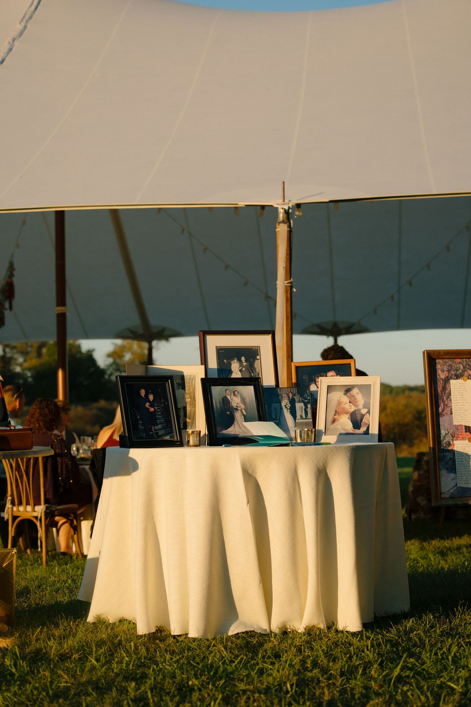 A round table with white tablecloth displays framed photographs under an outdoor tent at sunset.