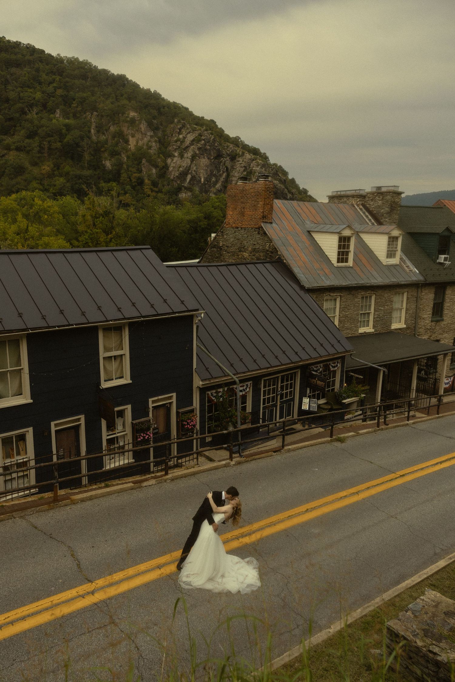 Bride and groom share a romantic dip kiss on a small-town street with historic buildings and a rocky mountain backdrop.