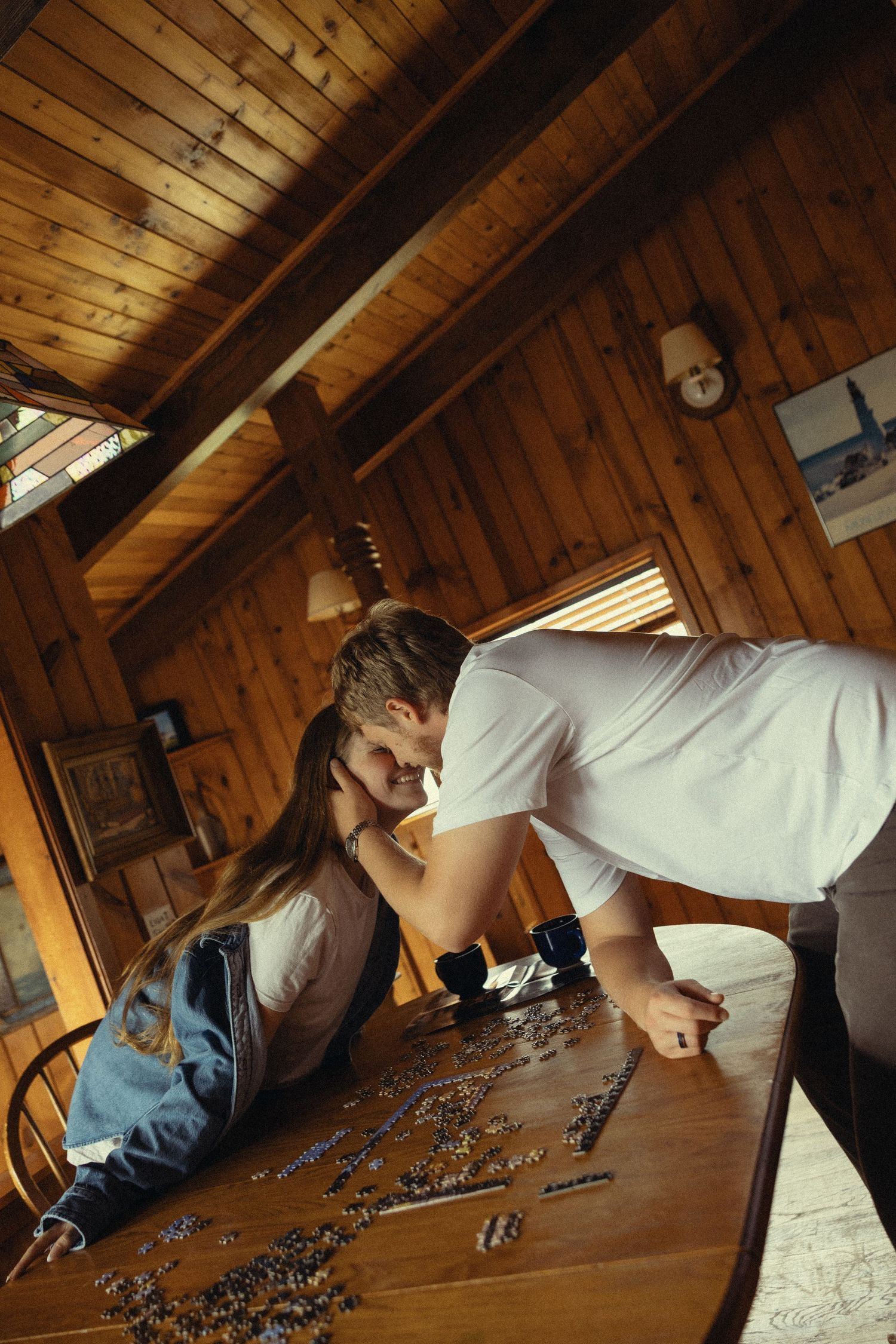 Couple sharing a romantic moment over a jigsaw puzzle at a wooden table in a cozy log cabin interior.