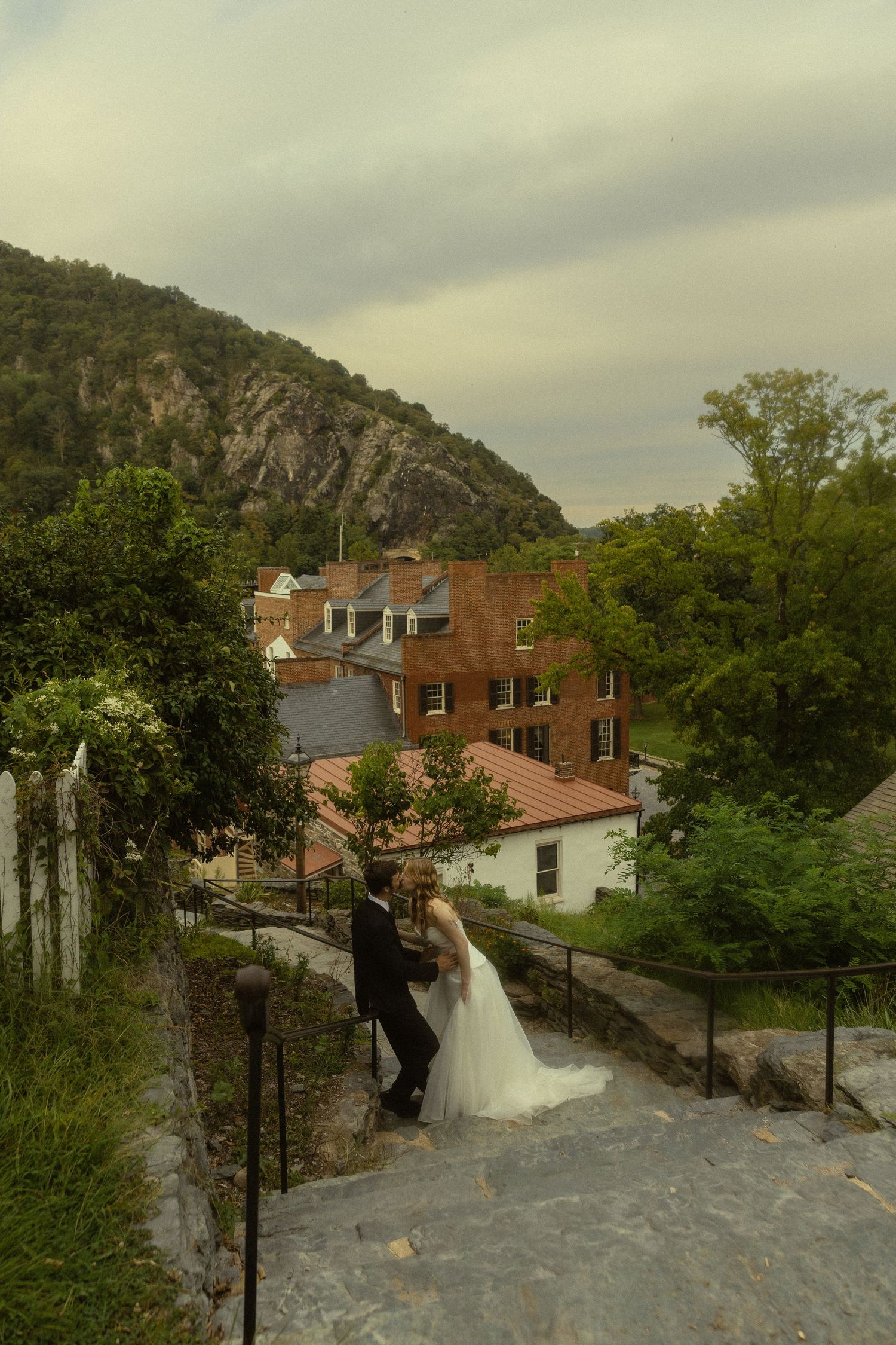 Bride and groom share a romantic moment on stone steps with a scenic mountain town backdrop on their wedding day.