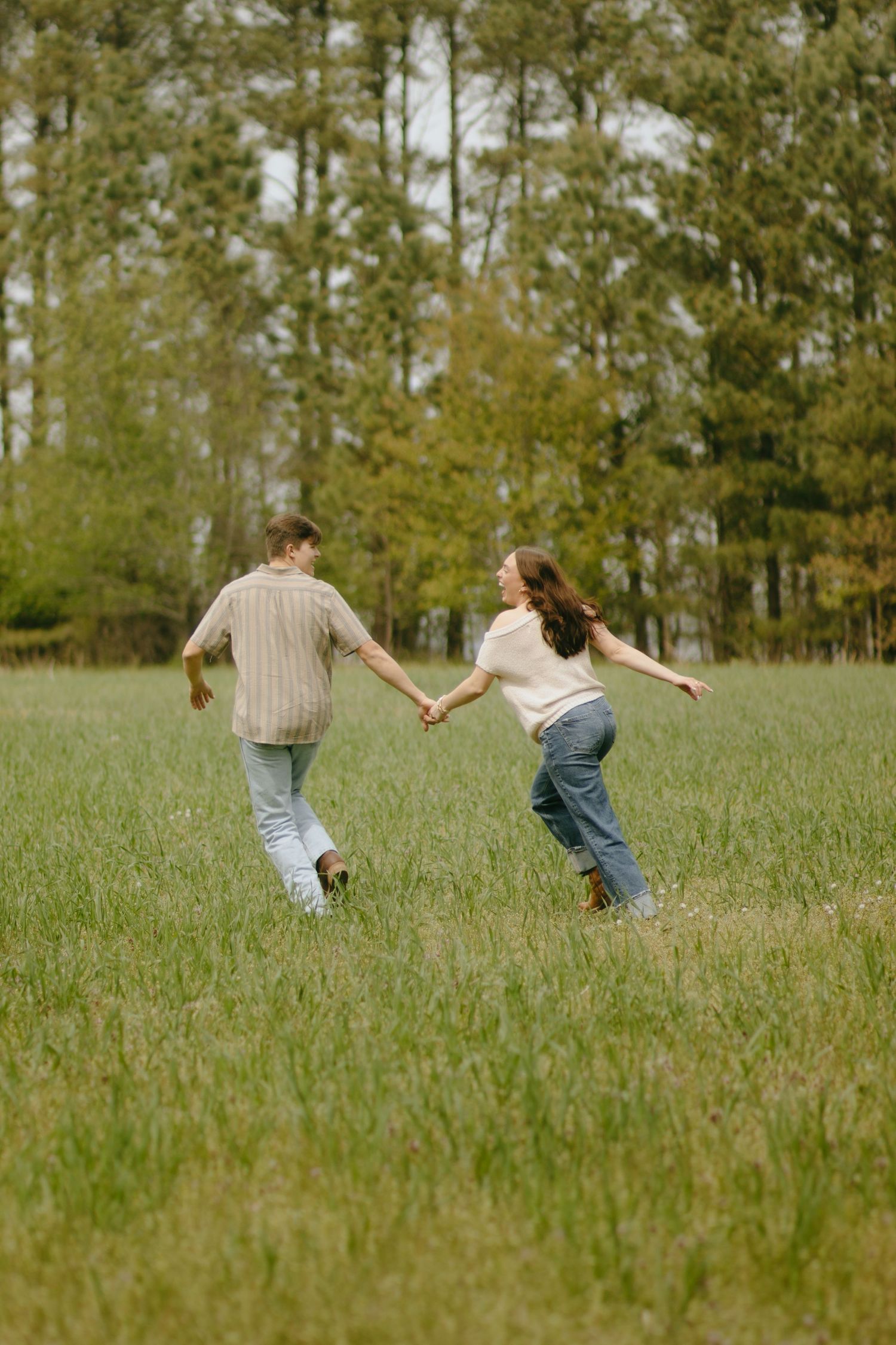 A playful couple running and holding hands in a green meadow.