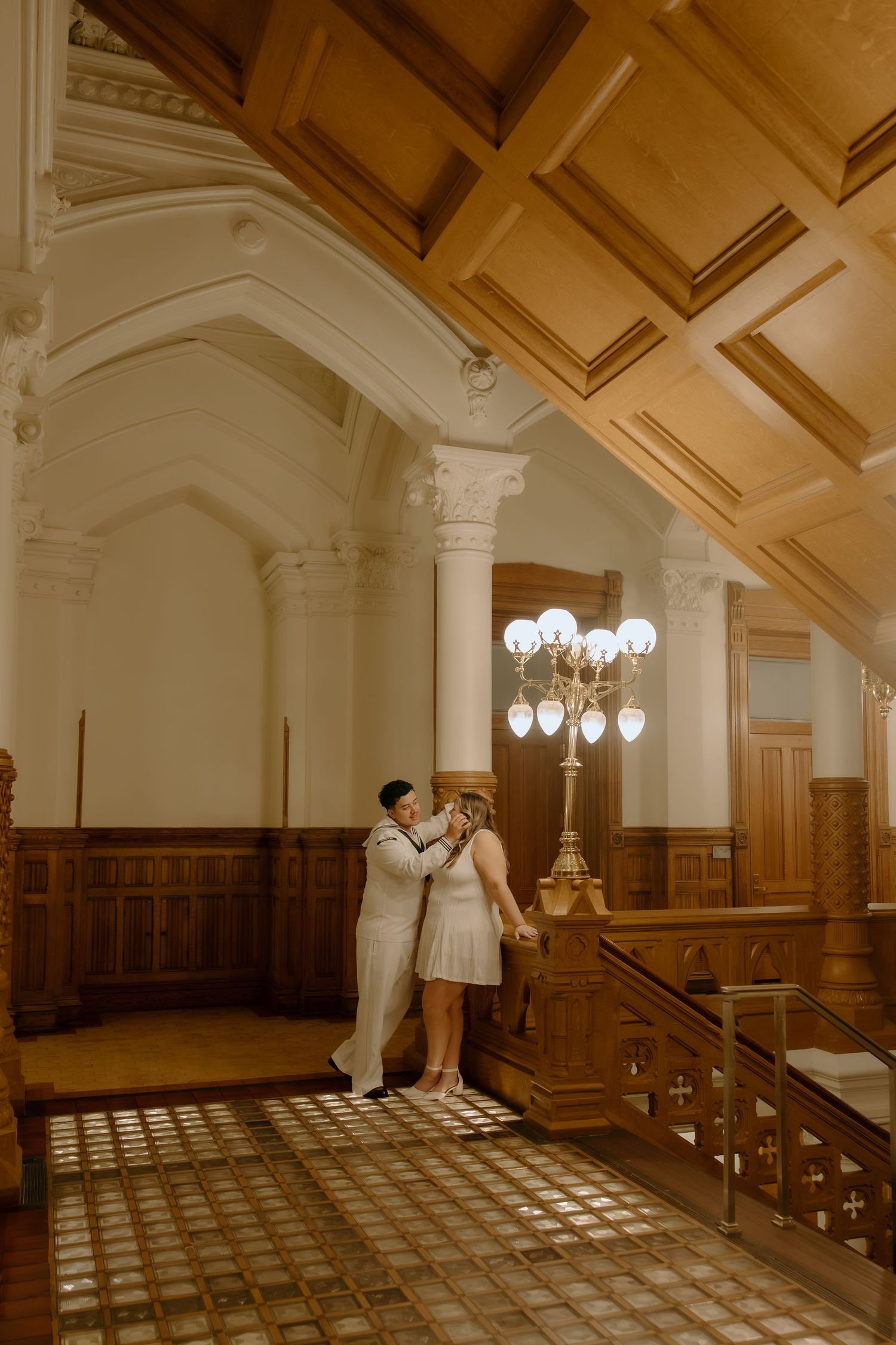 Couple sharing a romantic moment in an elegant historic building with ornate wooden ceiling and vintage chandelier.