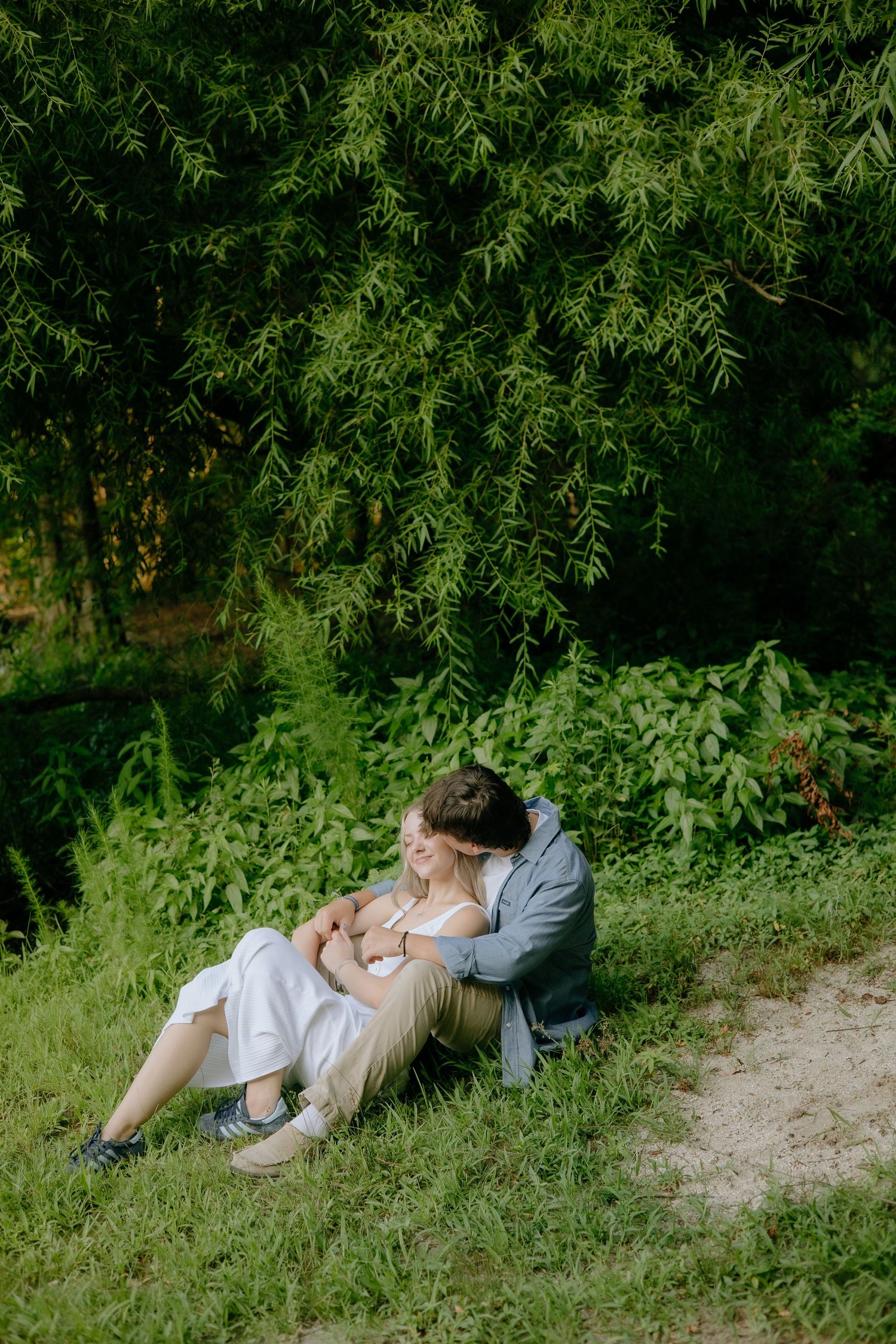 A couple lounges together on a grassy hillside surrounded by lush greenery.
